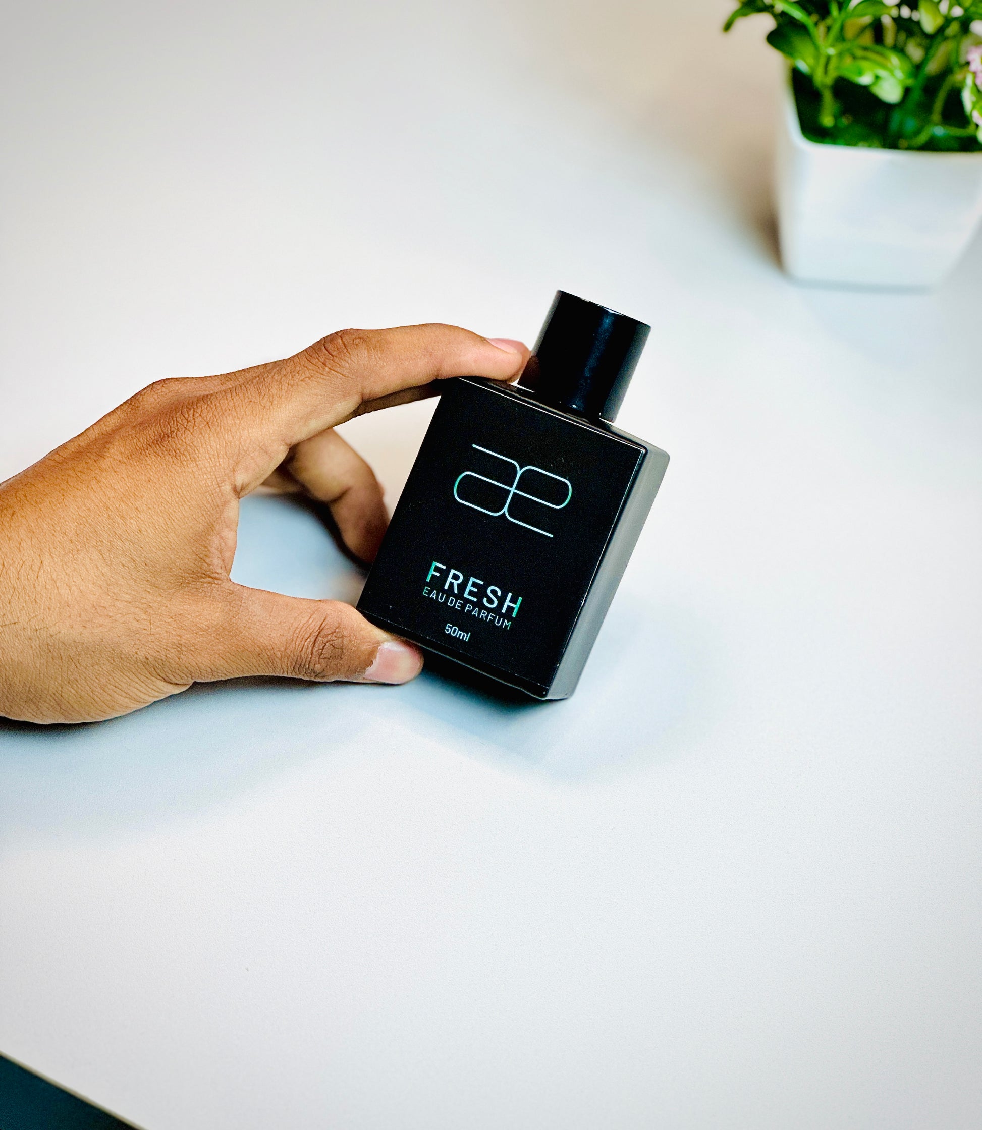 Hand holding Blaek Fresh Perfume (50ml) against a soft white background.