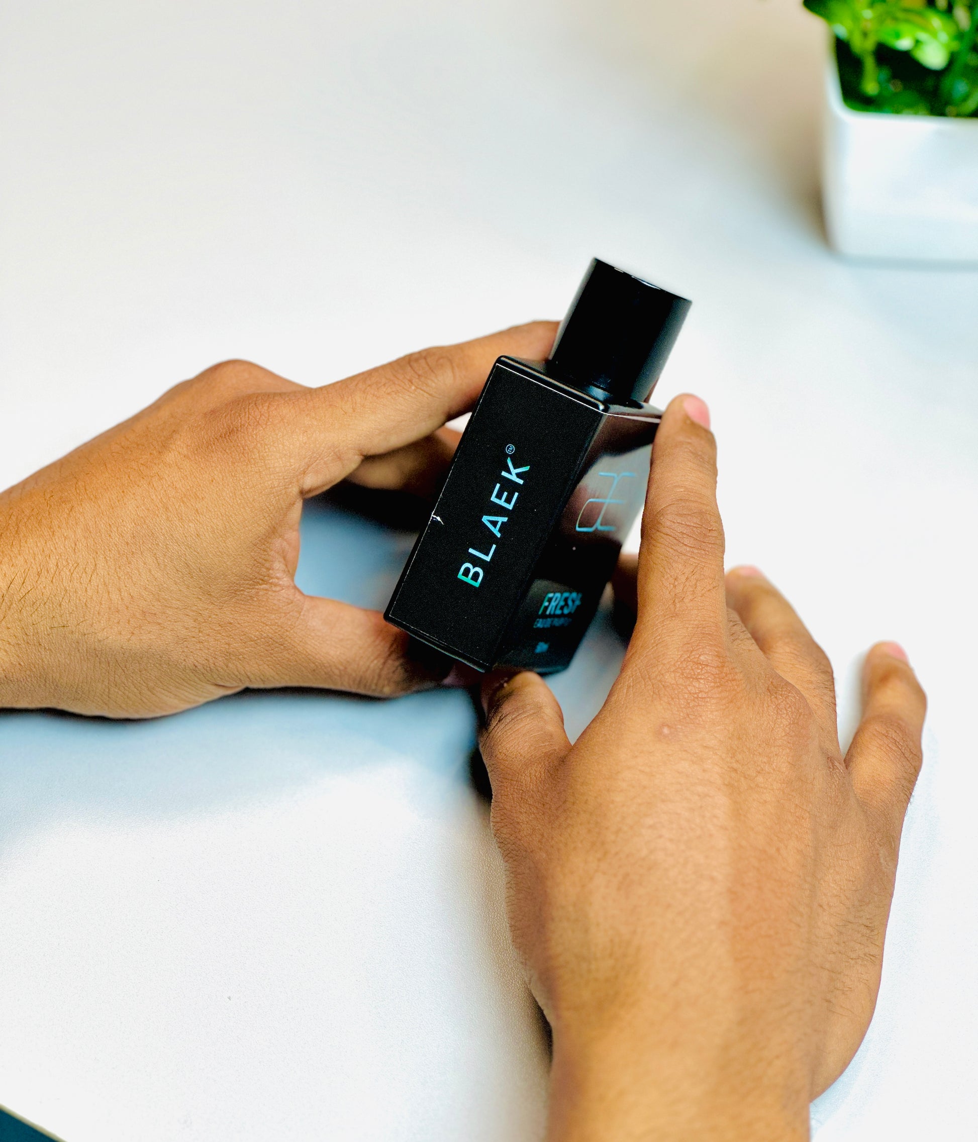 Blaek Fresh Perfume (50ml) gripped in hands with cap on for display.