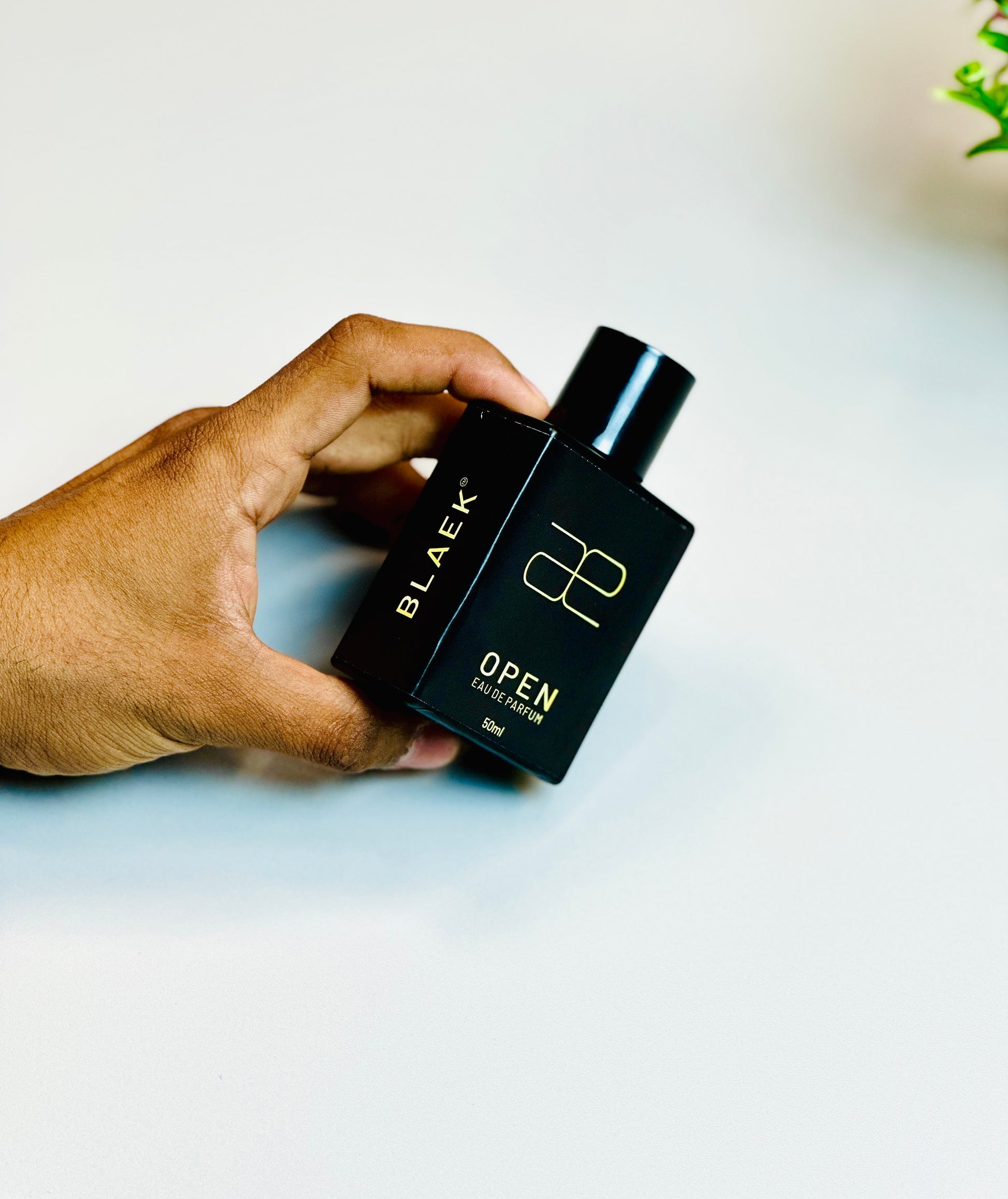 Blaek Open Perfume (50ml) gently held between fingers for product view.