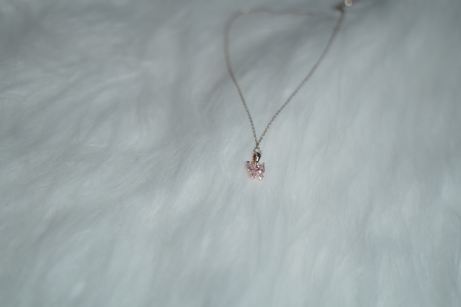 Blush Butterfly Necklace with rose pink stones placed on soft white fur.