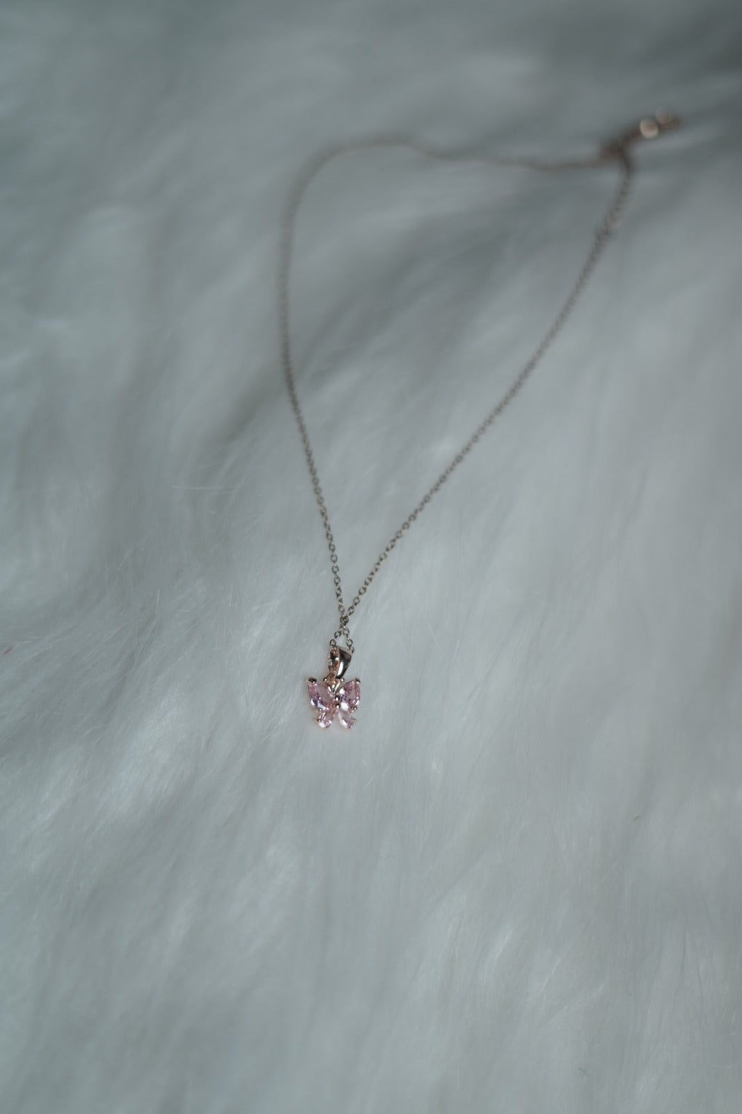 Feminine butterfly charm necklace with pink stones on white surface.