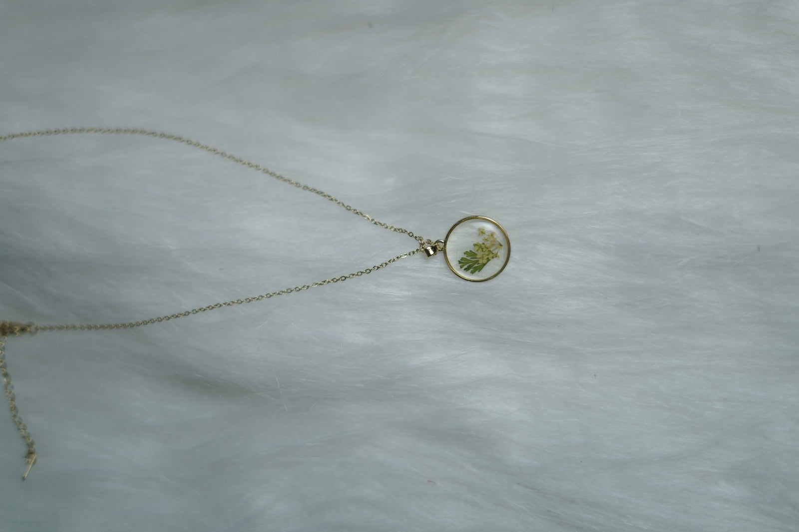 Gold chain necklace with resin floral pendant on minimal white surface.