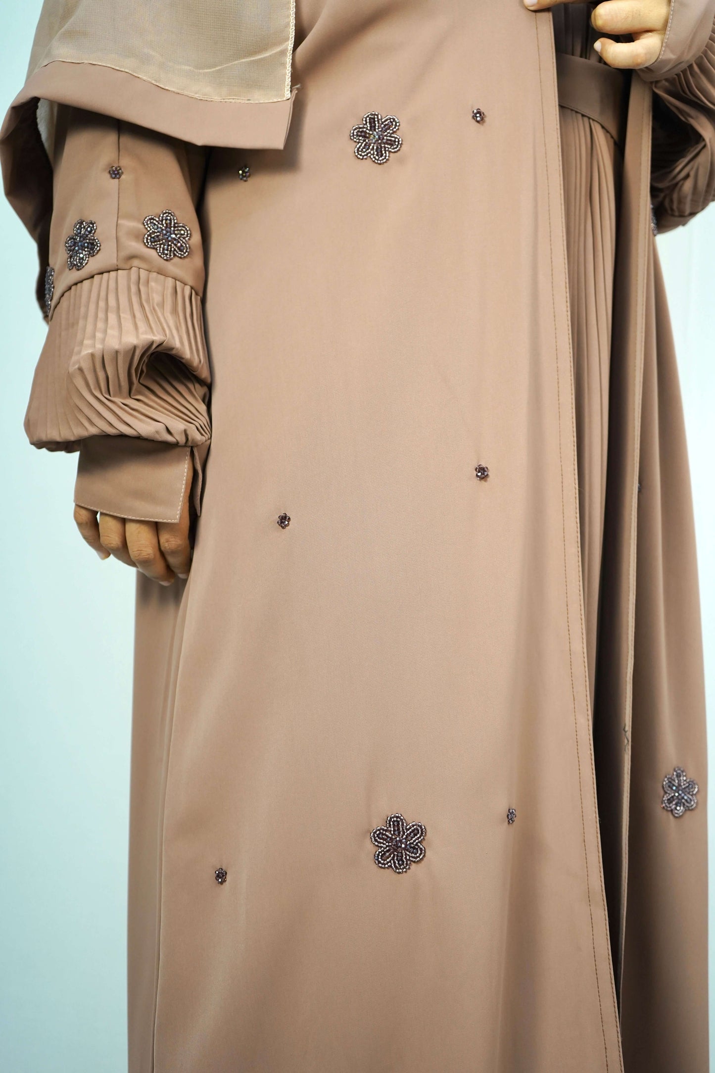 A close-up of a model wearing the brown abaya, highlighting the beaded floral embellishments and pleated sleeves.
