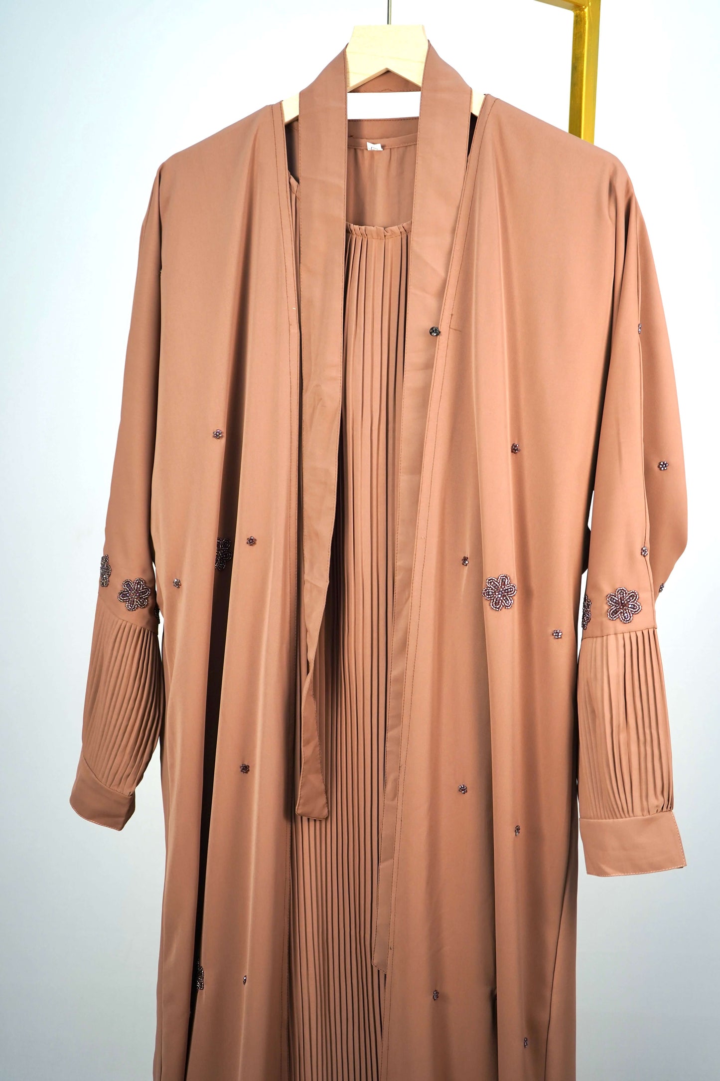 A close-up of the open-front design of the brown abaya, showing the smooth outer layer and the pleated inner dress.