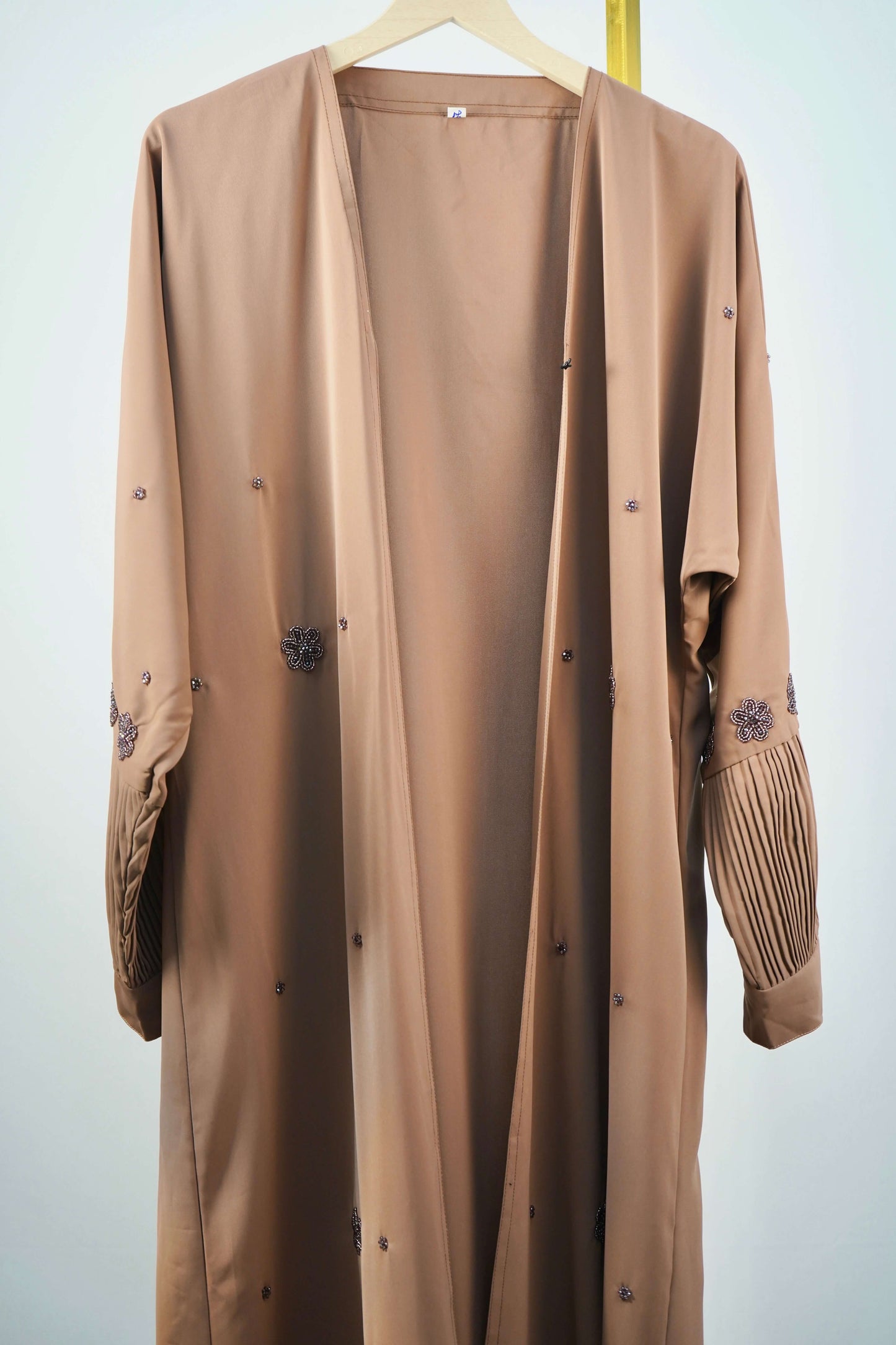 The brown Korean Alqa Nidha Abaya hanging open to showcase the design of the outer layer with its flowing drape and beaded details.
