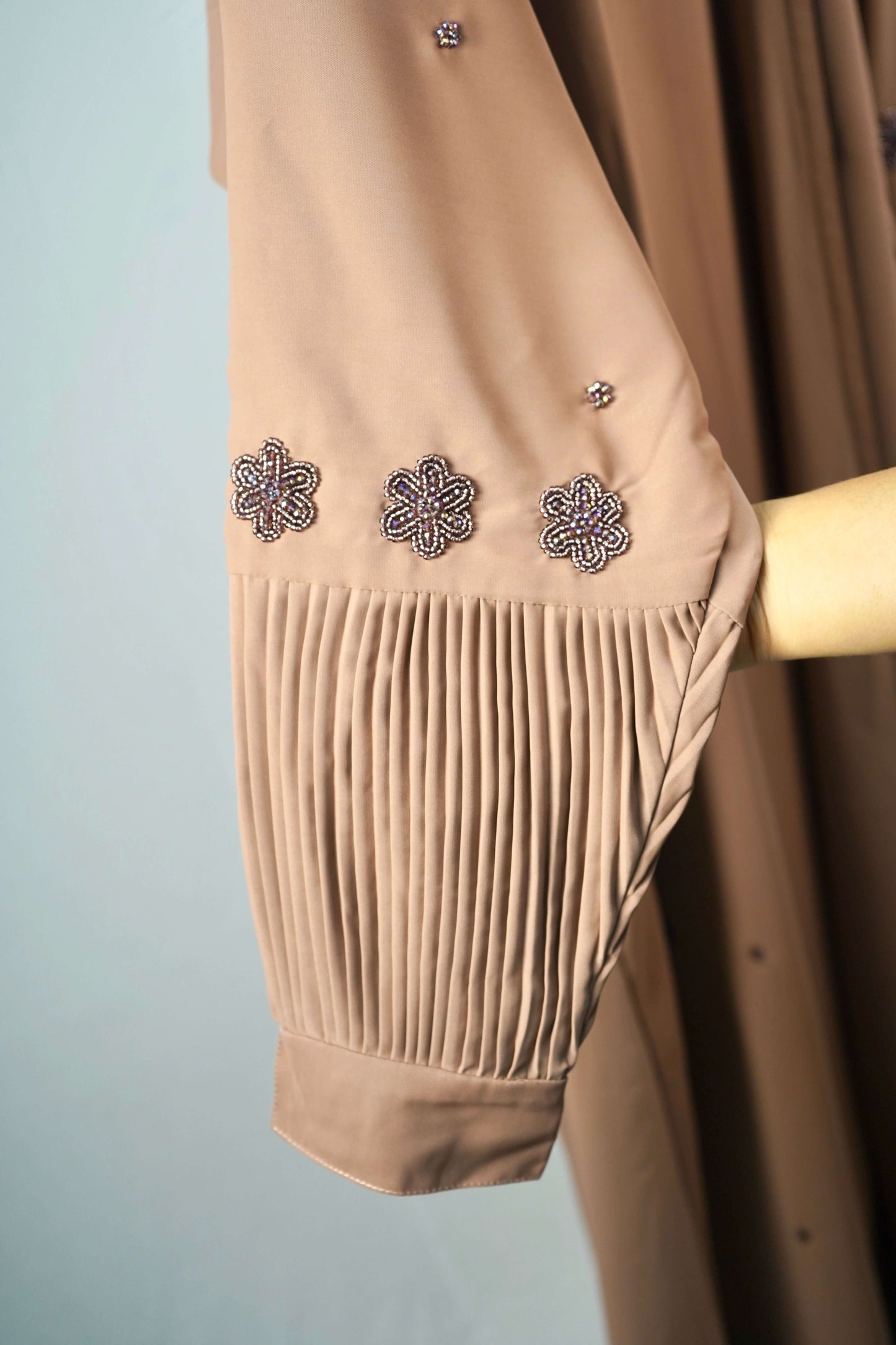 A close-up of the pleated cuff and the beaded floral design on the sleeve of the brown abaya.