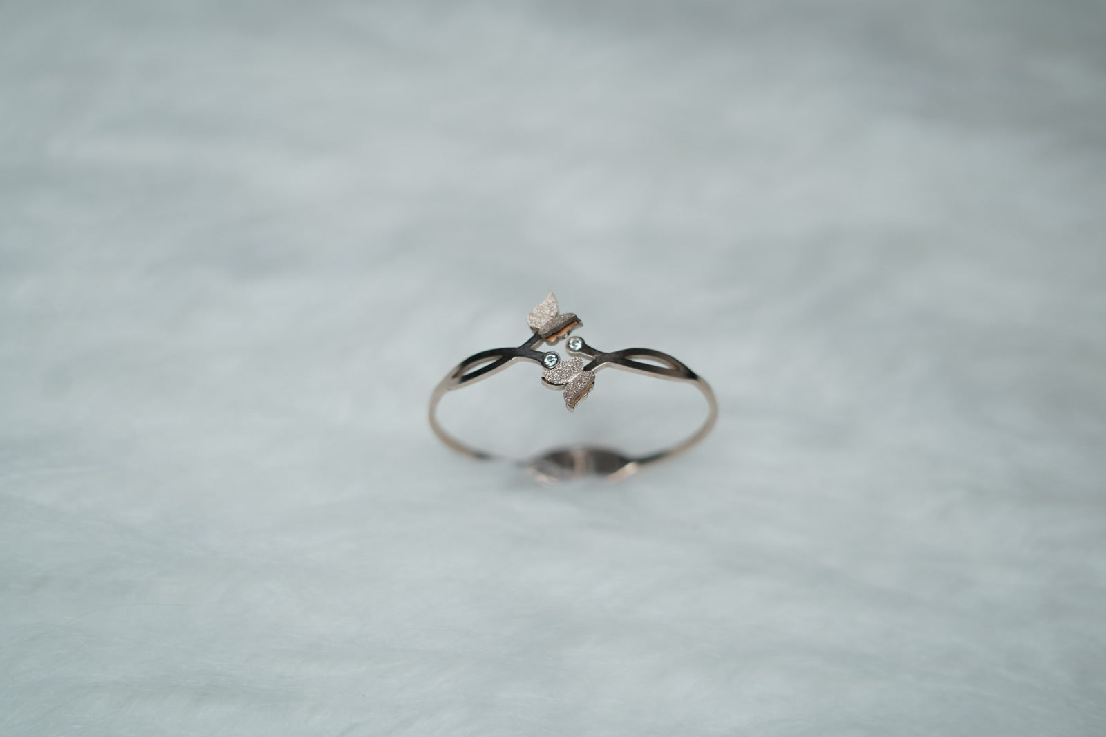 Romantic gold bangle with butterfly and crisscross loop design on minimal background.