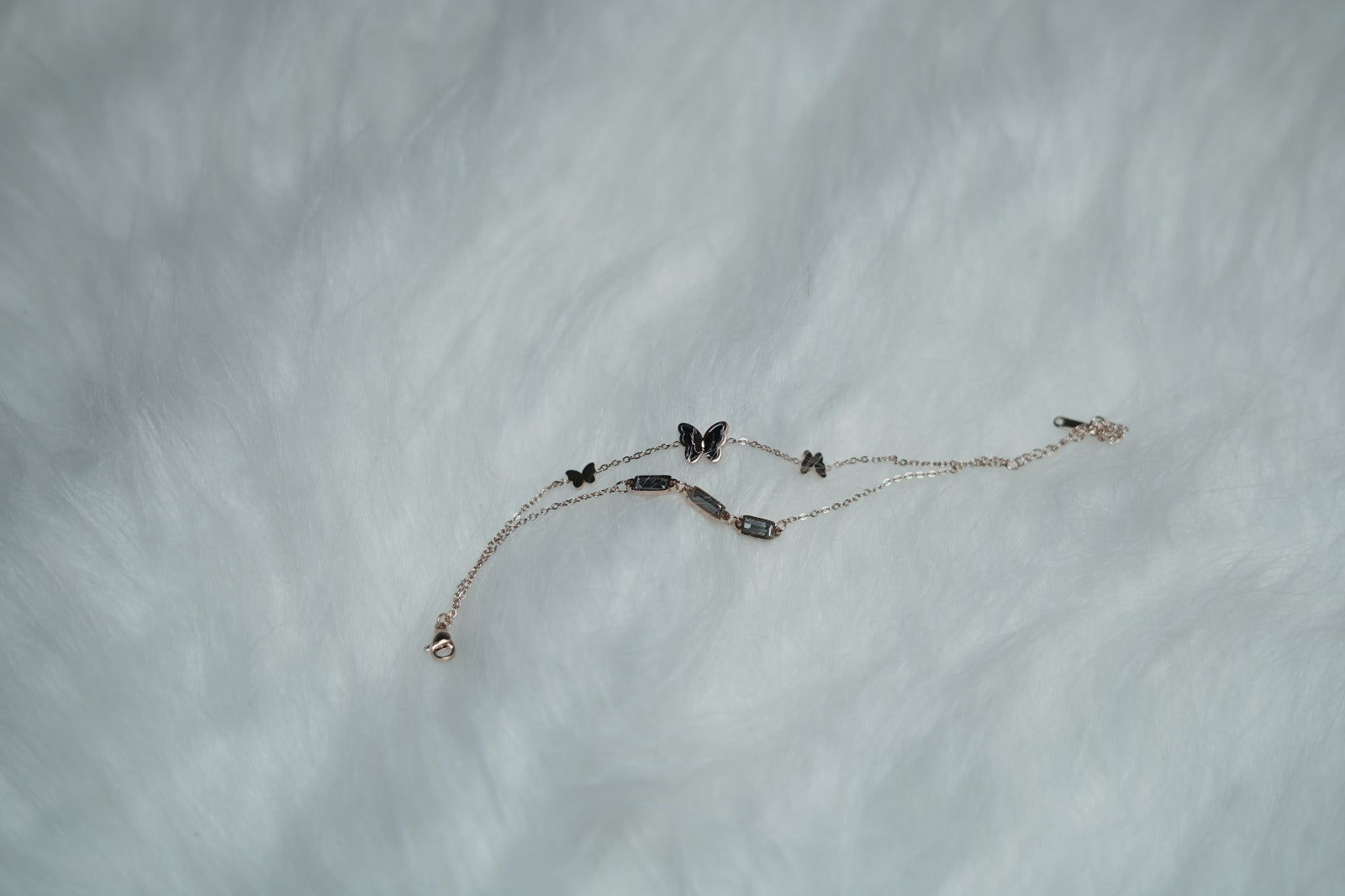 Flatlay of butterfly bracelet resting on fluffy white fur, highlighting soft-toned elegance.