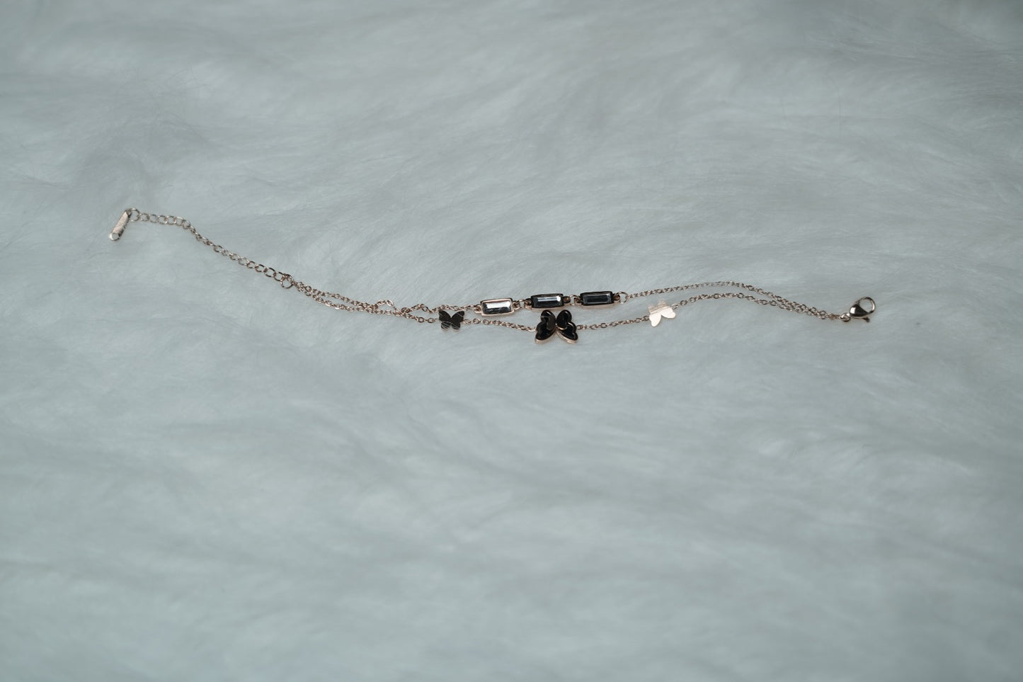 Butterfly Garden Bracelet laid flat on white fur, showcasing double chains and clear accents.