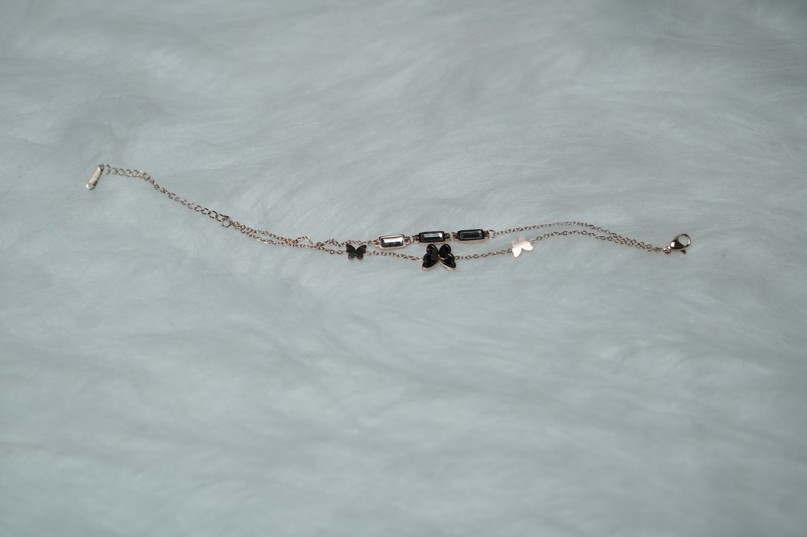 Butterfly Garden Bracelet laid flat on white fur, showcasing double chains and clear accents.