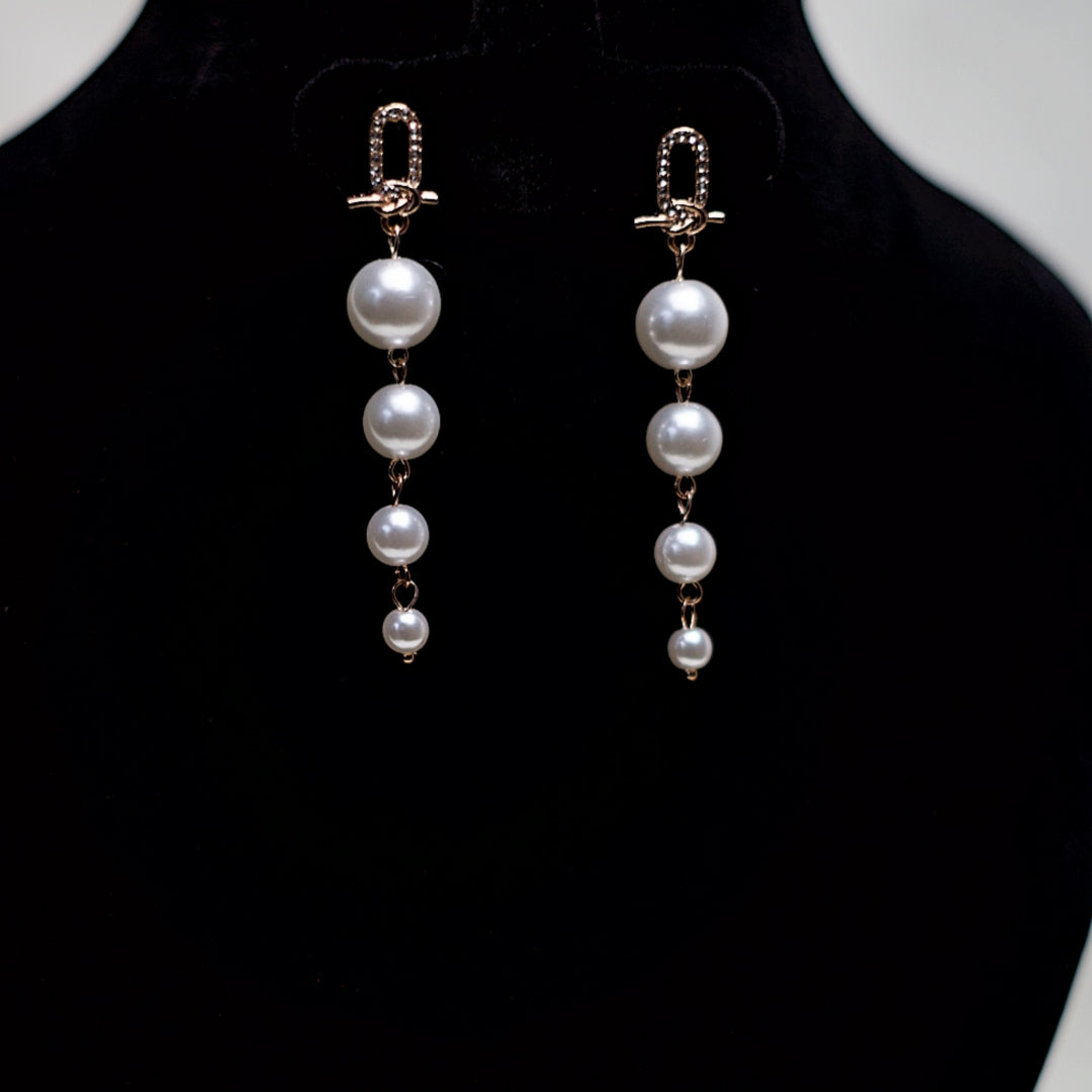 Close-up of rose gold-tone dangle earrings featuring detailed crystal-studded links and a cascade of glossy white pearls in a modern vertical design.