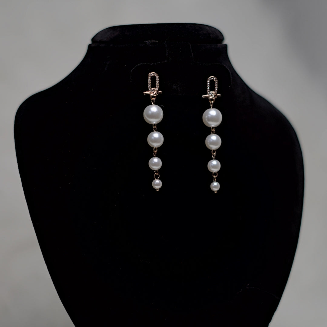 Elegant long pearl earrings hanging from crystal-embellished loop studs, with four white pearls in descending size, displayed against a black background.