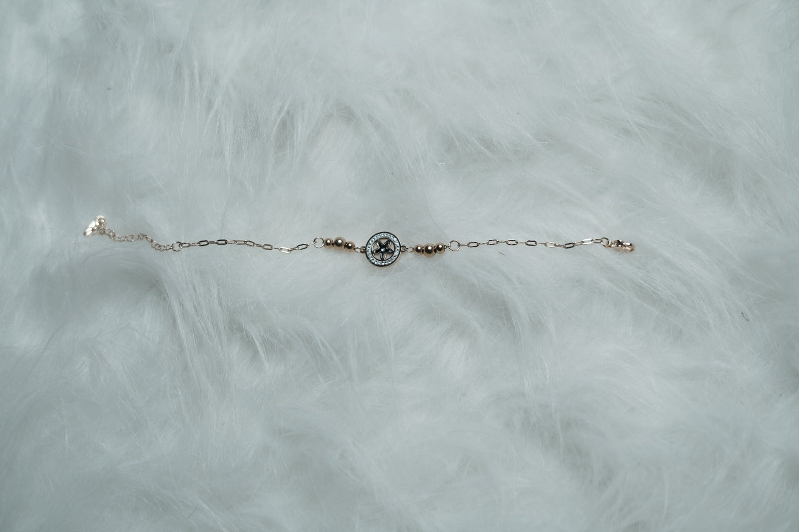 A rose gold compass charm bracelet displayed on soft white fur, with beaded detailing on both sides.