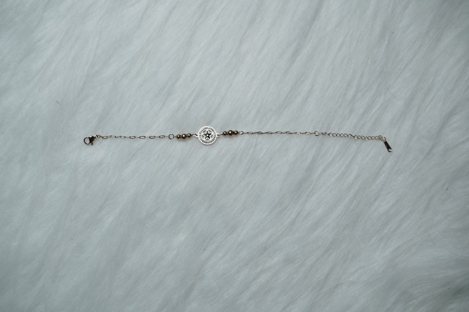 A symbolic star-inspired bracelet placed neatly on soft white fur, featuring a round compass charm.