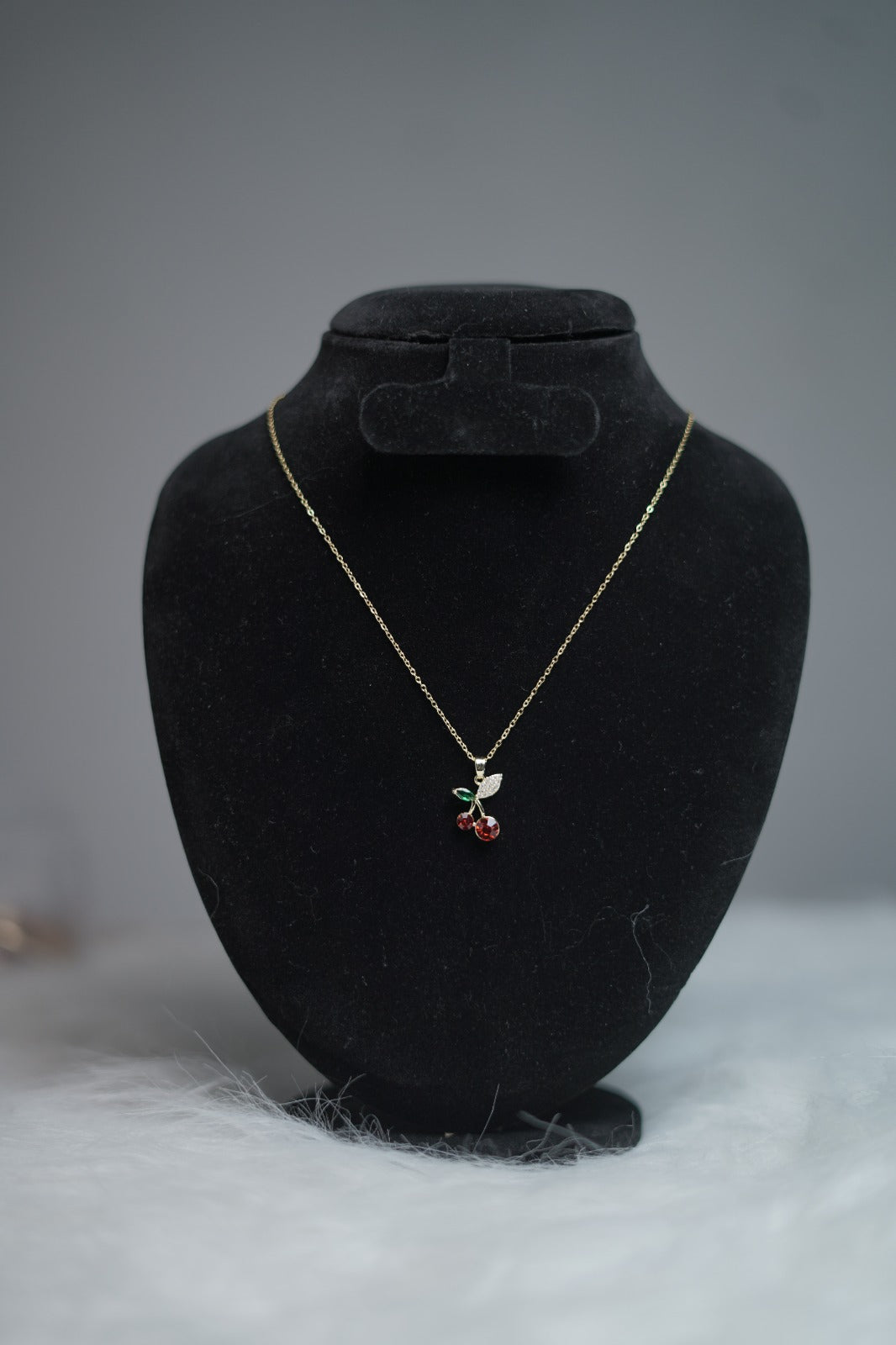 Cute cherry fruit pendant necklace shown on jewelry stand.