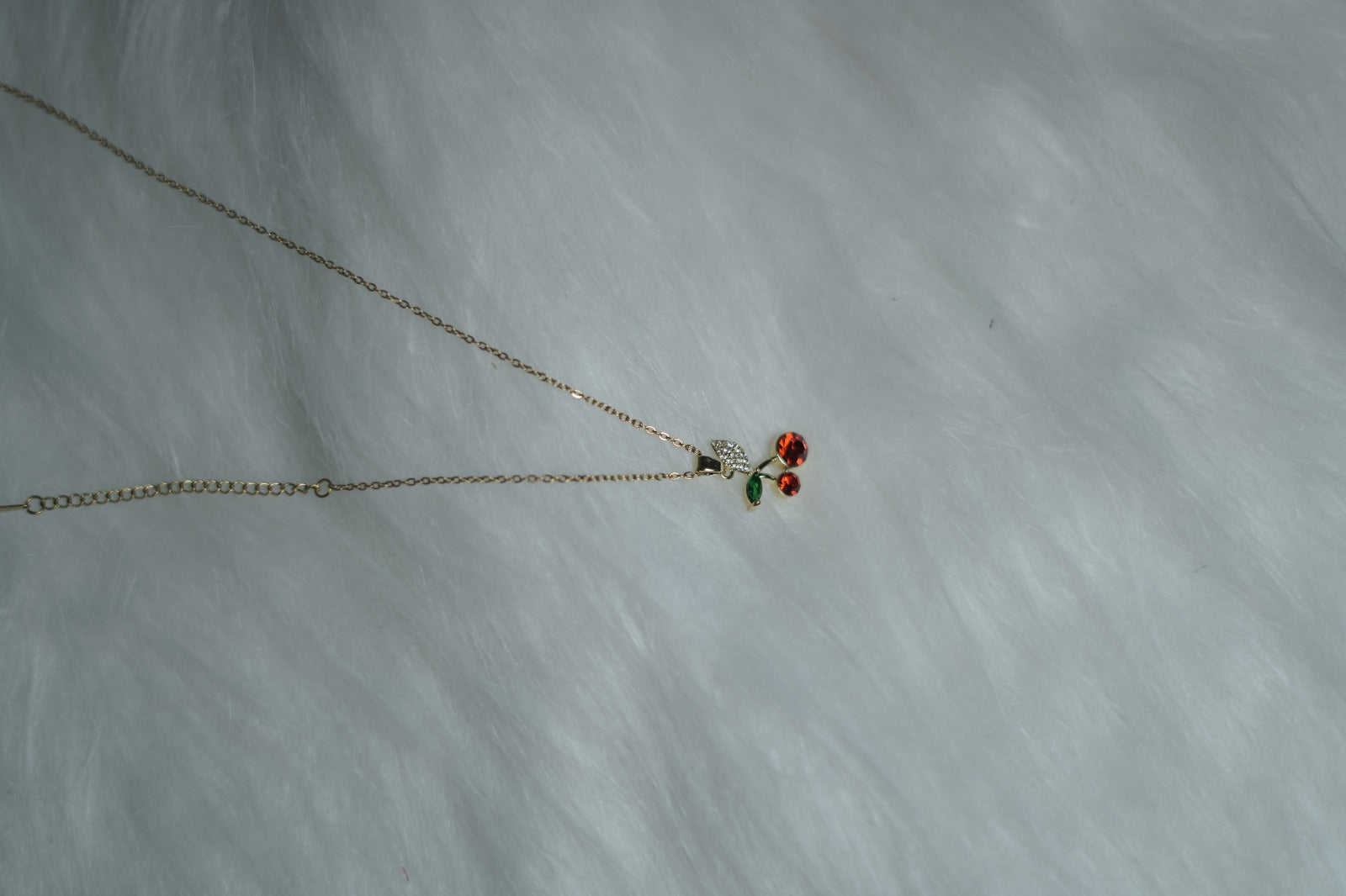 Red and green crystal cherry necklace laid on white background.