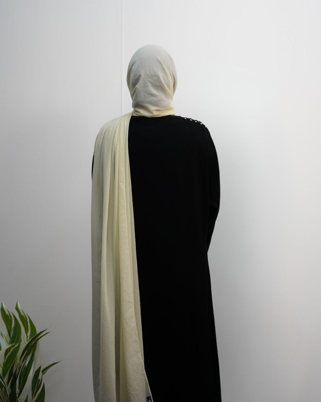 Back view of woman wearing cream indian chiffon hijab draped over black abaya.