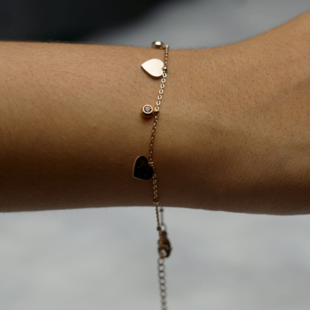 Rose gold bracelet with heart and crystal charms on wrist.