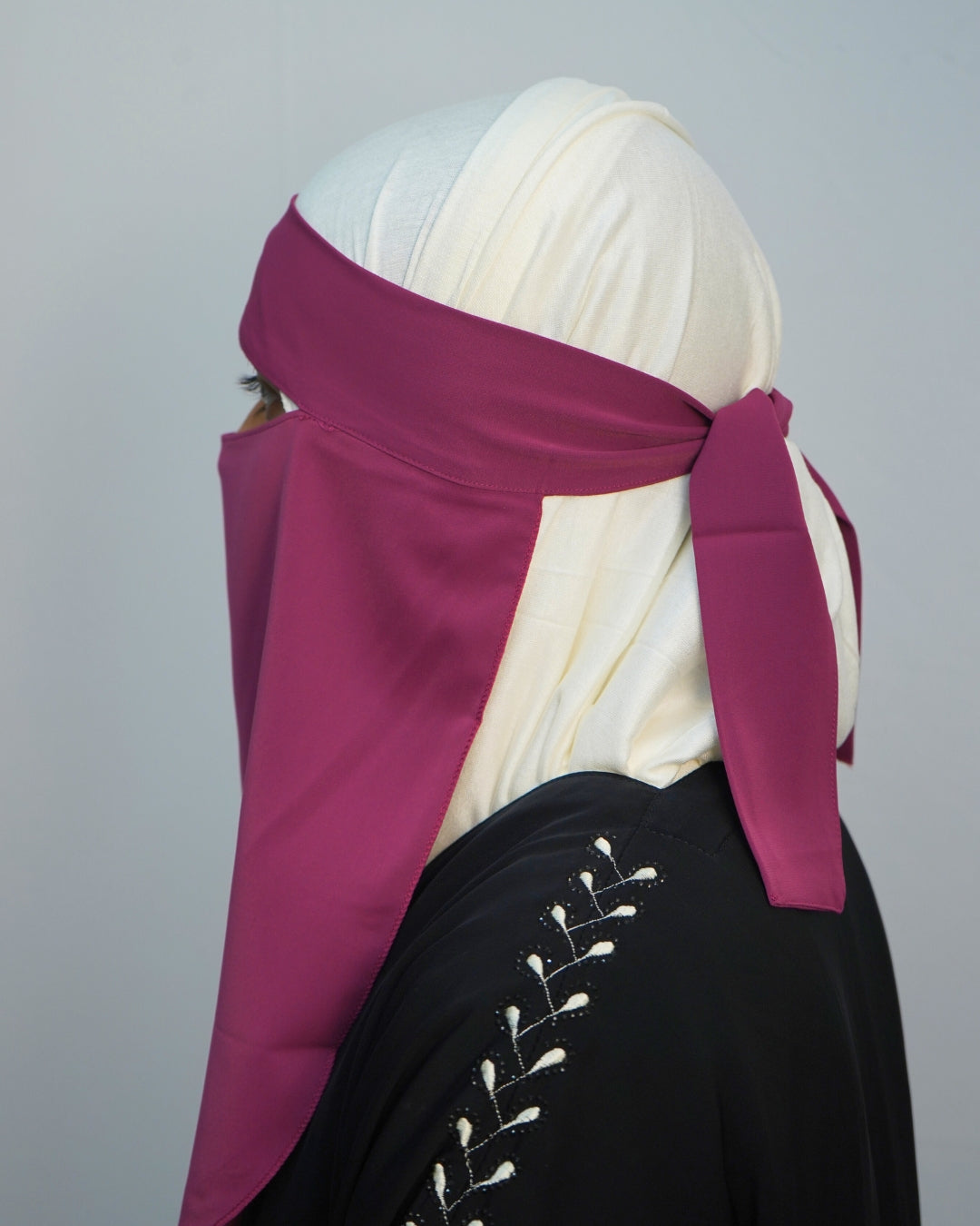 Side profile of deep magenta chiffon niqab with adjustable tie-back.