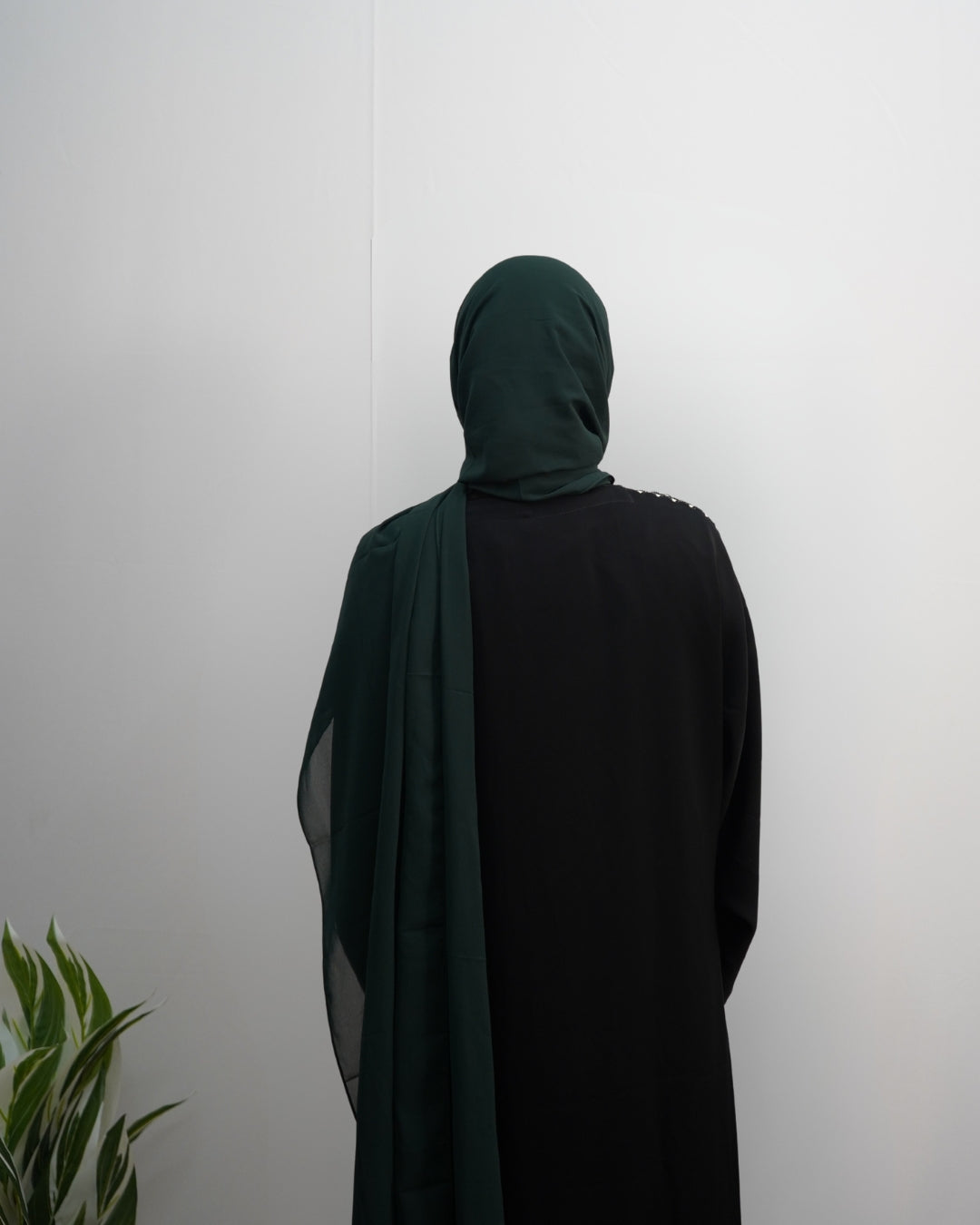 Woman wearing a deep green indian chiffon hijab styled with a black abaya, back view.