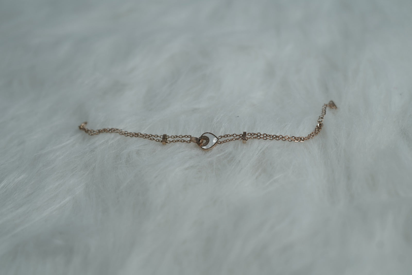 Bracelet showcasing a central orbit heart pendant and delicate double chains on a soft background.