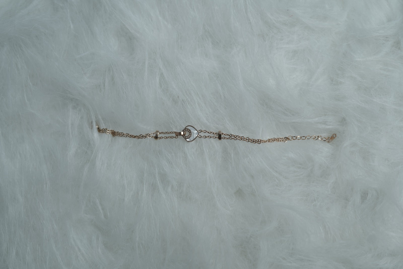 Dual-chain bracelet featuring a center heart-in-ring design, displayed on a furry white surface.