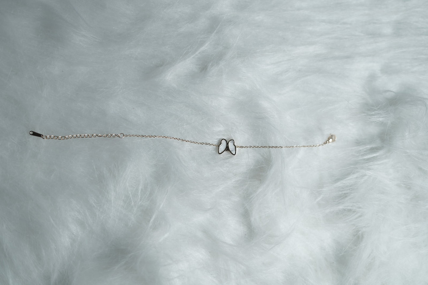 Rose gold bracelet with the white butterfly side featured, resting on fur.