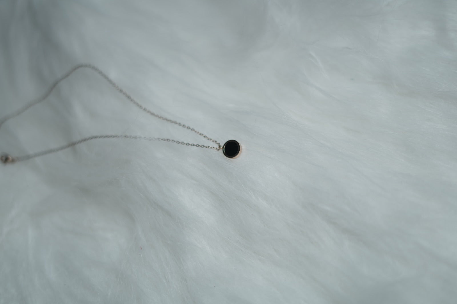 Reversible gold pendant showing black side, styled on white fur.