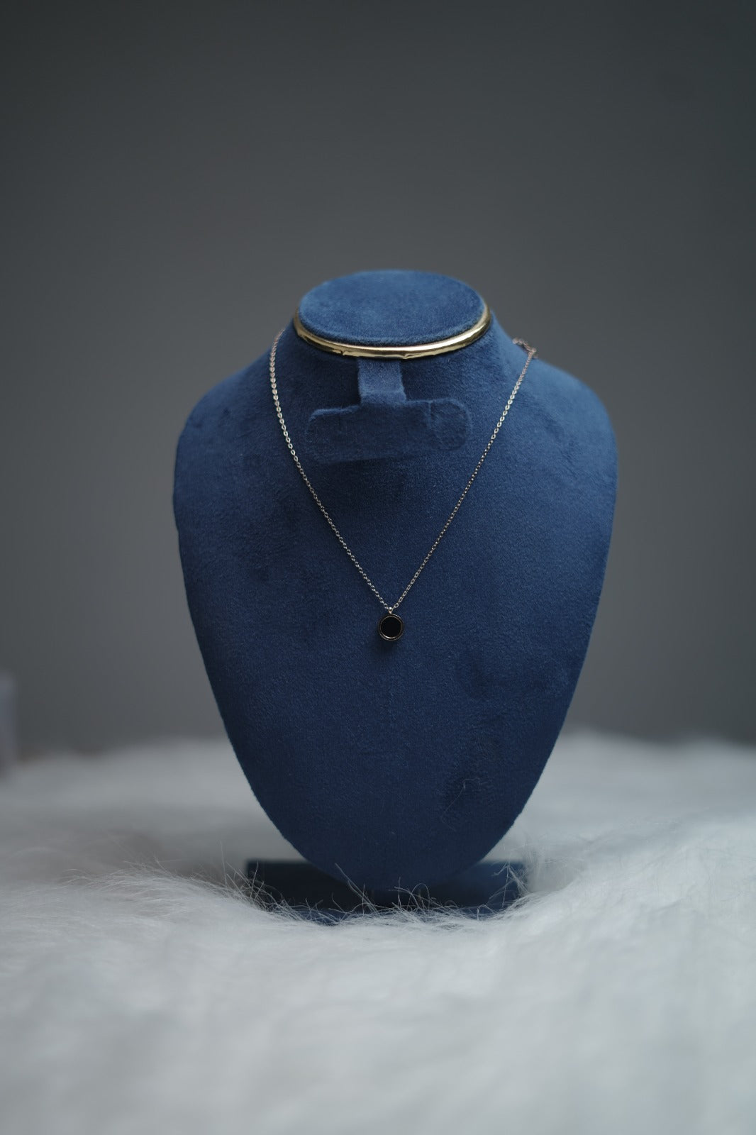 Necklace with glossy black face shown draped on jewelry stand.