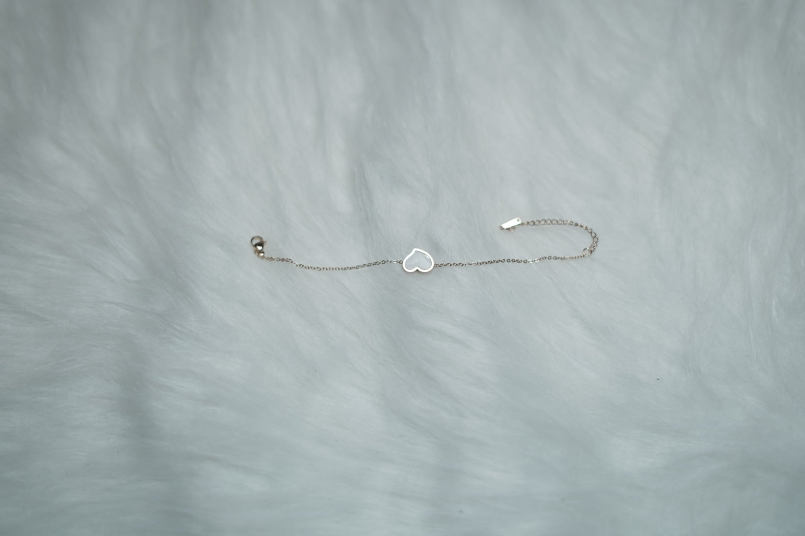 Chain bracelet featuring the white heart side, placed against a soft fabric background.