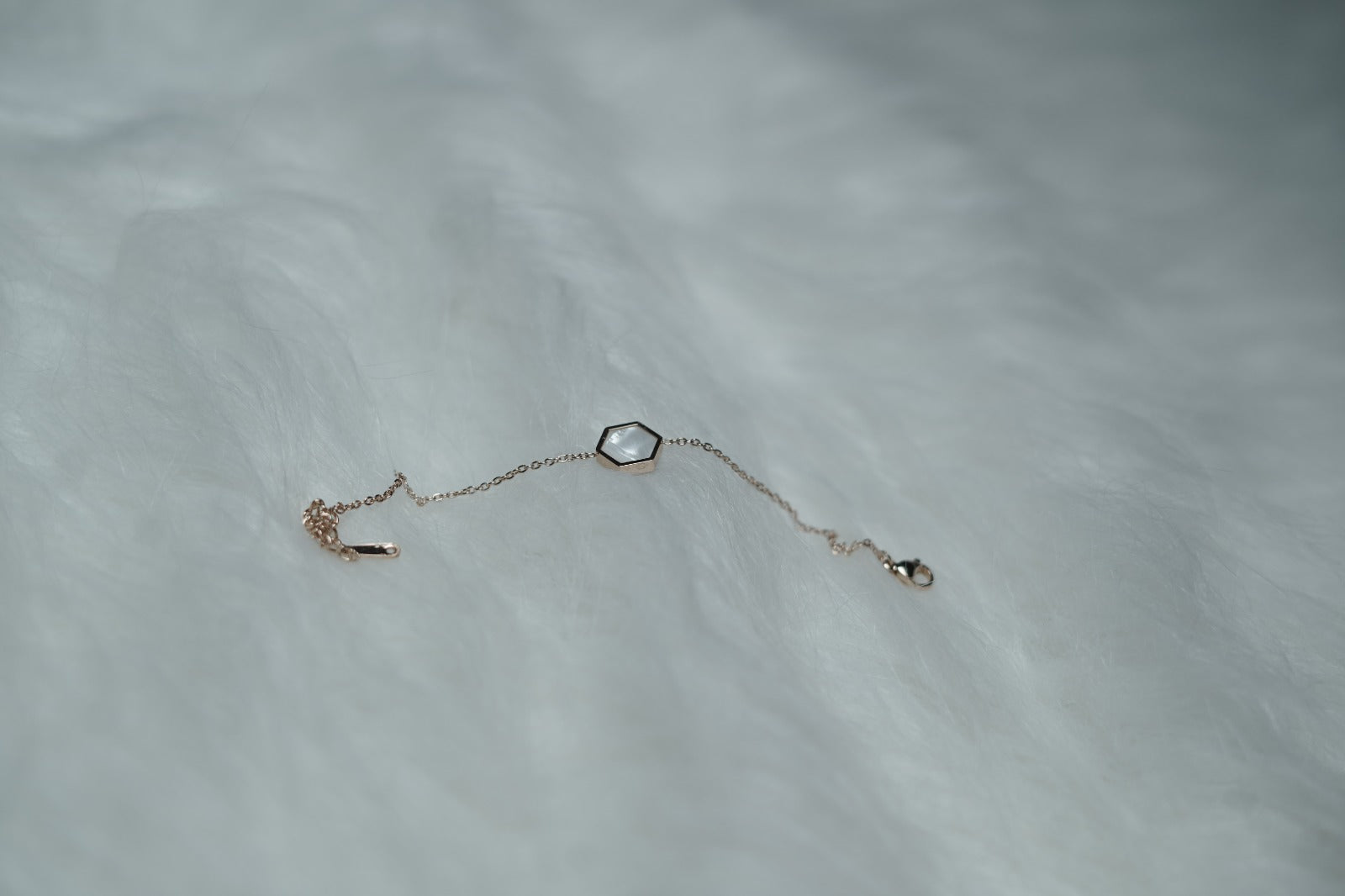 Rose gold chain bracelet featuring the white hexagon side on a textured surface.