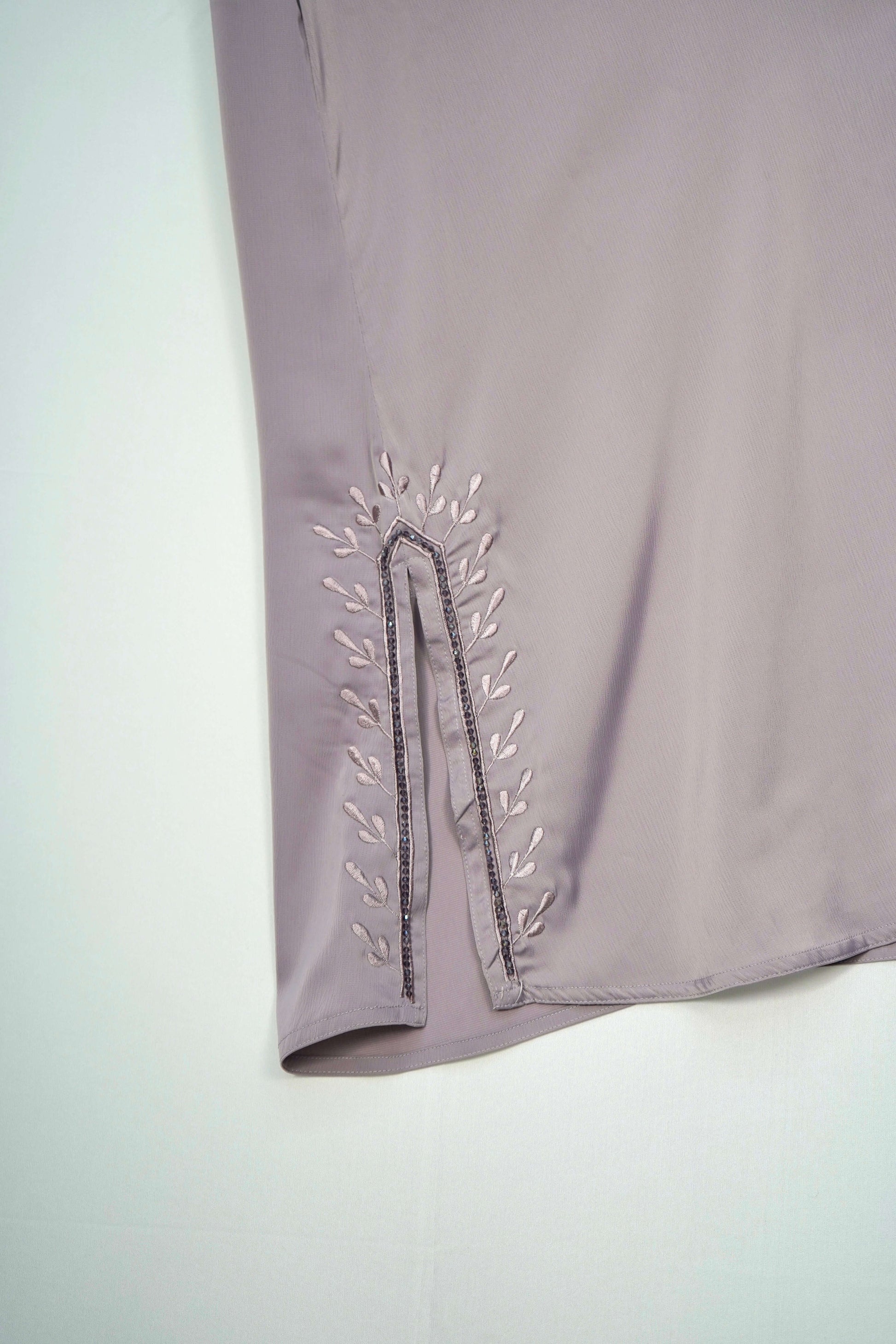 A close-up of the leaf-like embroidery and side slit on the dusty purple abaya.
