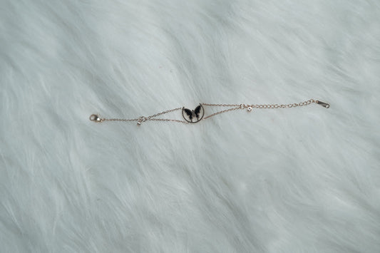 Rose gold-tone bracelet with a butterfly wing charm in a circular frame, laid out on a soft white fur surface.
