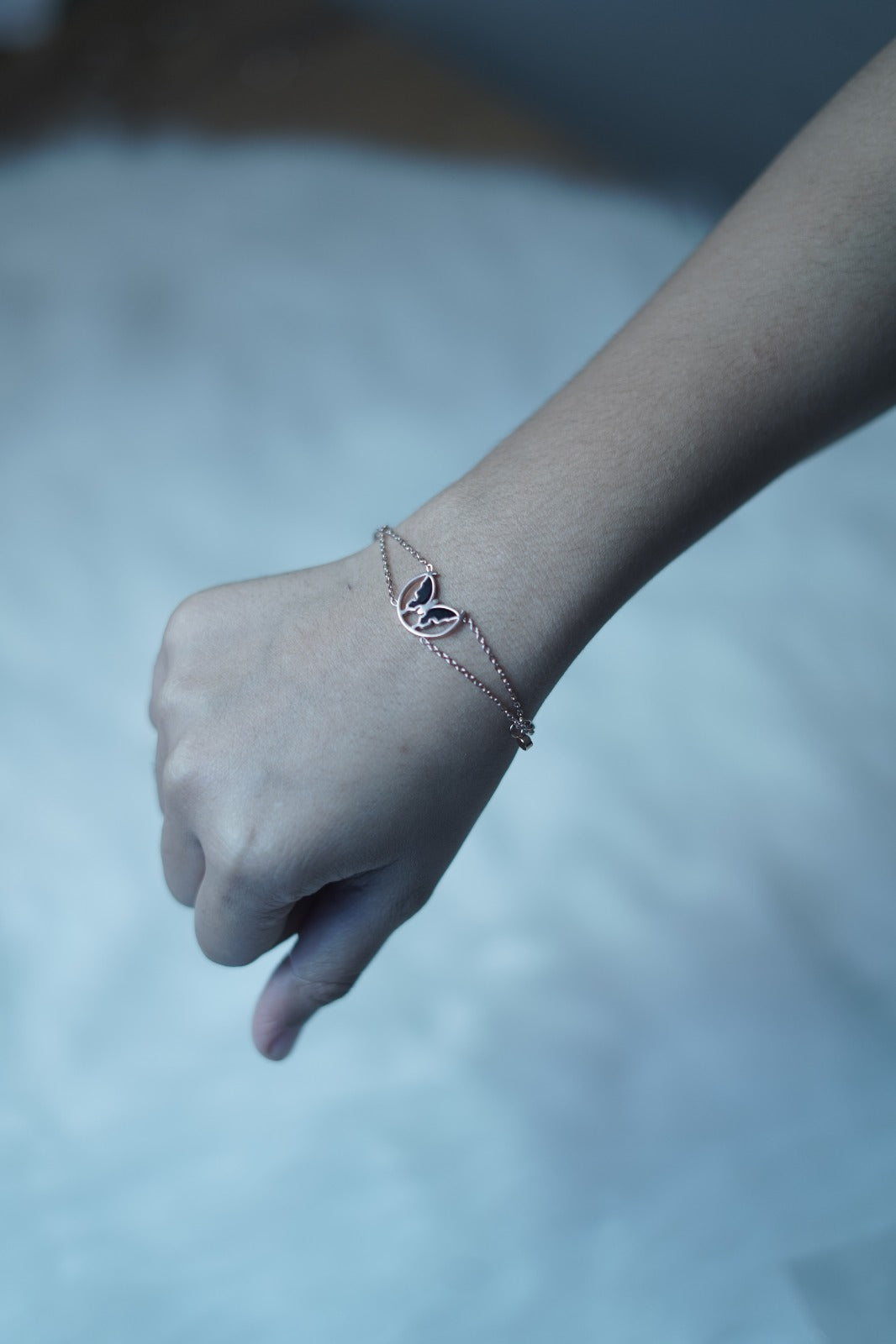 The Eclipsed Wings Bracelet worn on a wrist, showcasing its elegant butterfly charm and rose gold double-strand chain resting lightly on the skin.