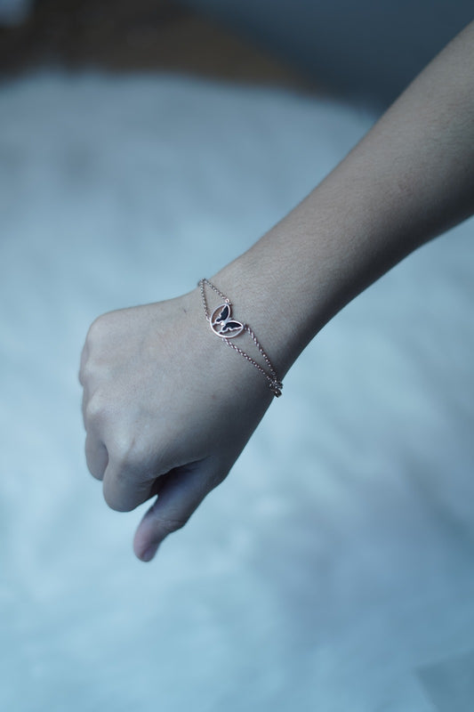 The Eclipsed Wings Bracelet worn on a wrist, showcasing its elegant butterfly charm and rose gold double-strand chain resting lightly on the skin.