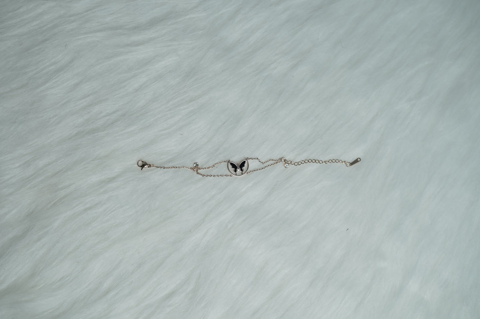 A dainty rose gold bracelet laid flat on soft fur, highlighting the butterfly pendant.