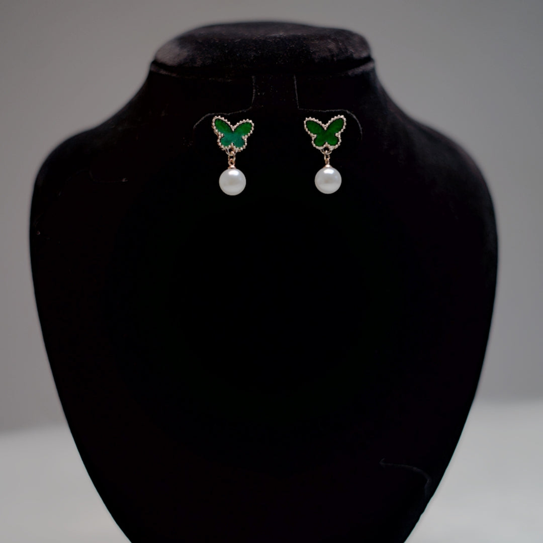Emerald green butterfly and pearl earrings mounted on a black velvet display, showcasing their vibrant enamel and rose gold accents.