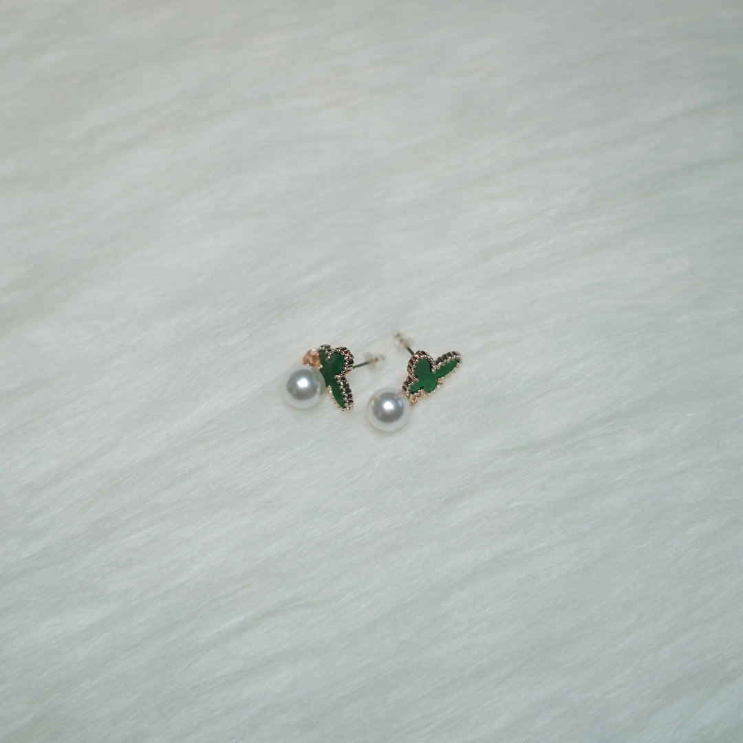 A pair of rose gold-trimmed green butterfly earrings with pearl drops, placed on a soft white background.