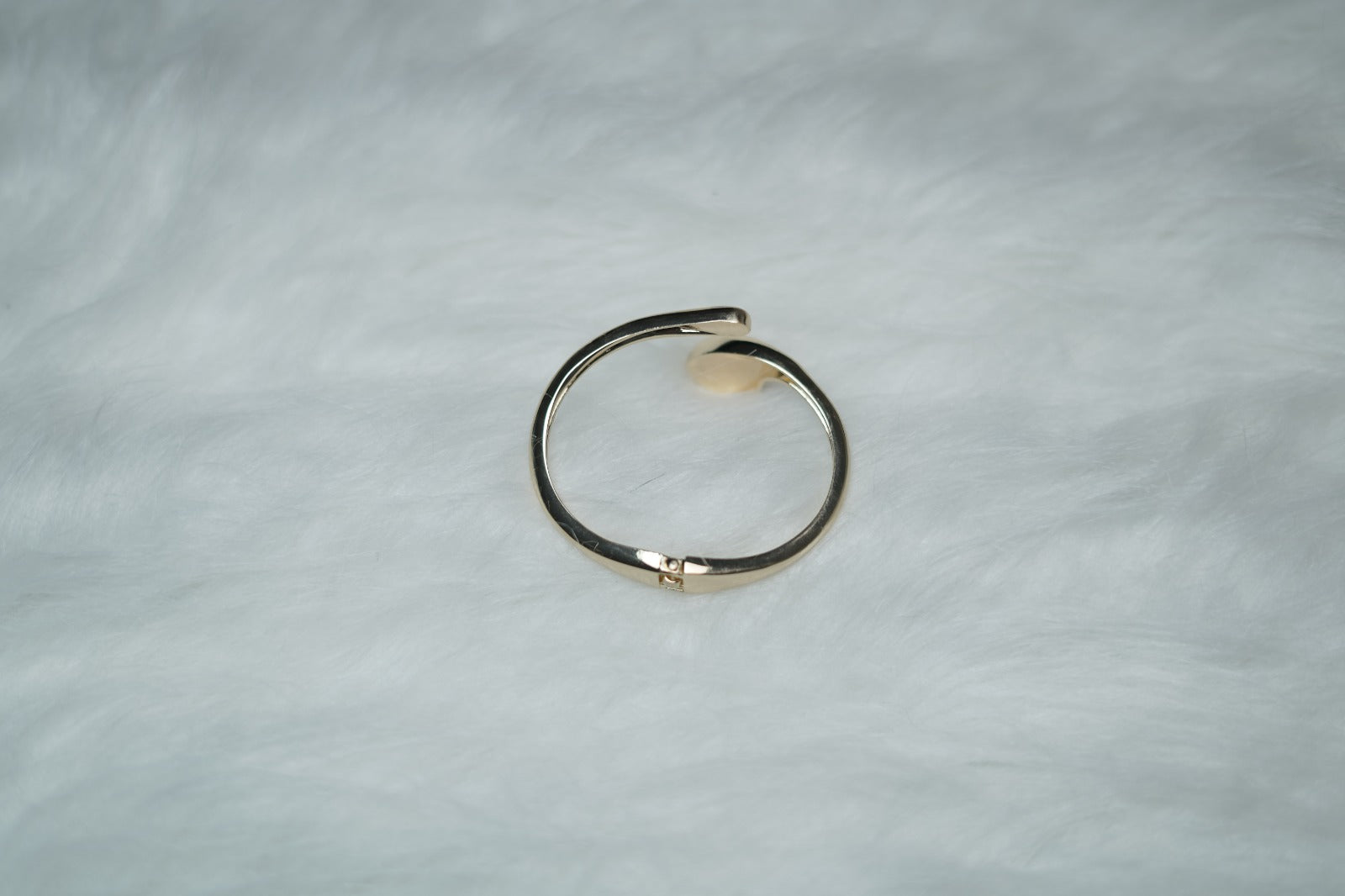 Hand wearing gold sculptural bangle with futuristic open-ended droplet design.