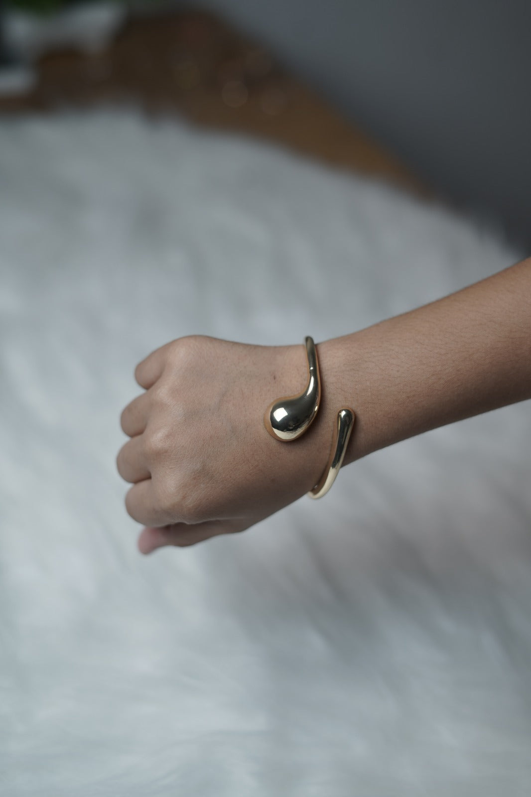Hand wearing fluid form bangle with futuristic open-ended droplet design.