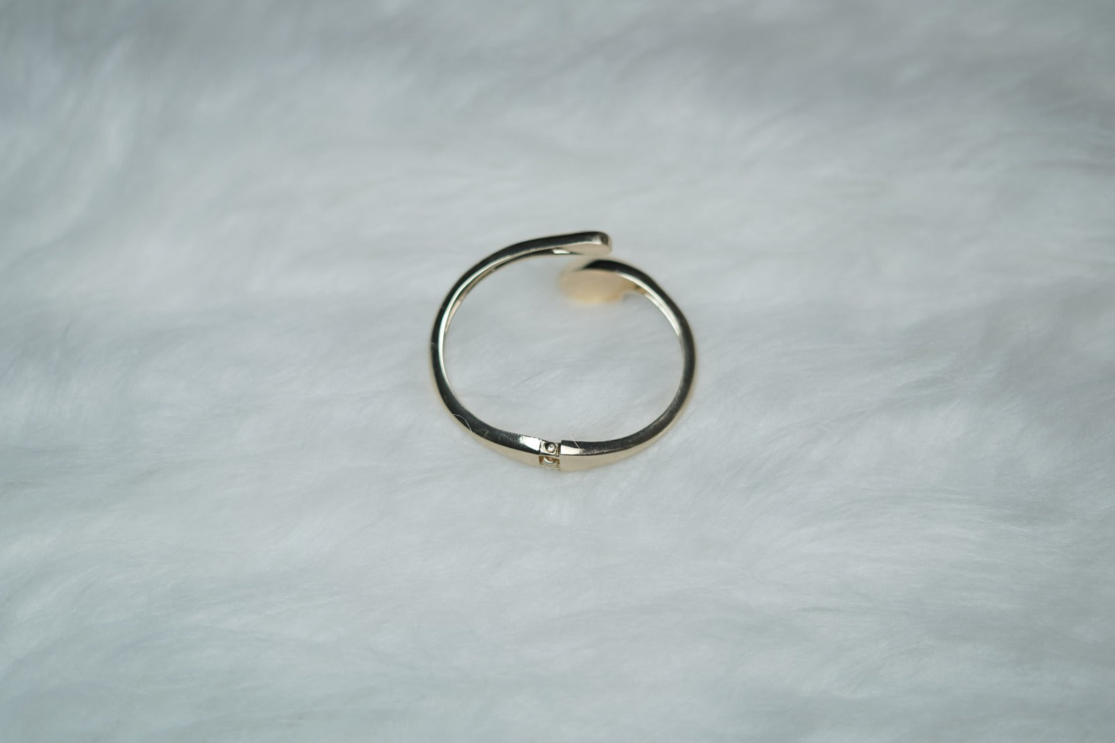 Modern gold cuff fluid form bracelet with molten swirl ends on plain surface.