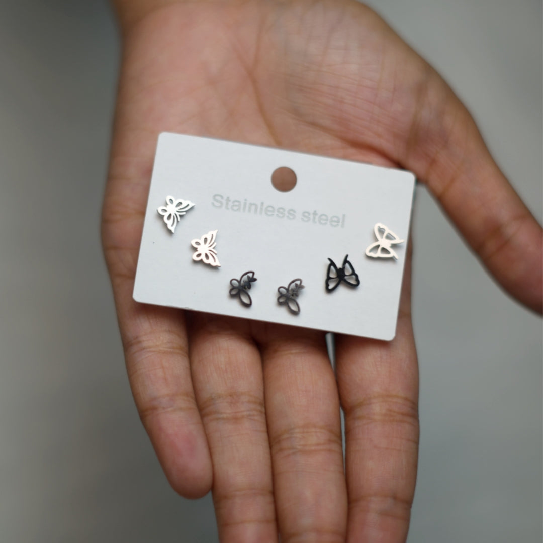 A trio of butterfly-shaped stud earrings in silver-tone alloy with unique cutout designs, placed on a neutral earring card.