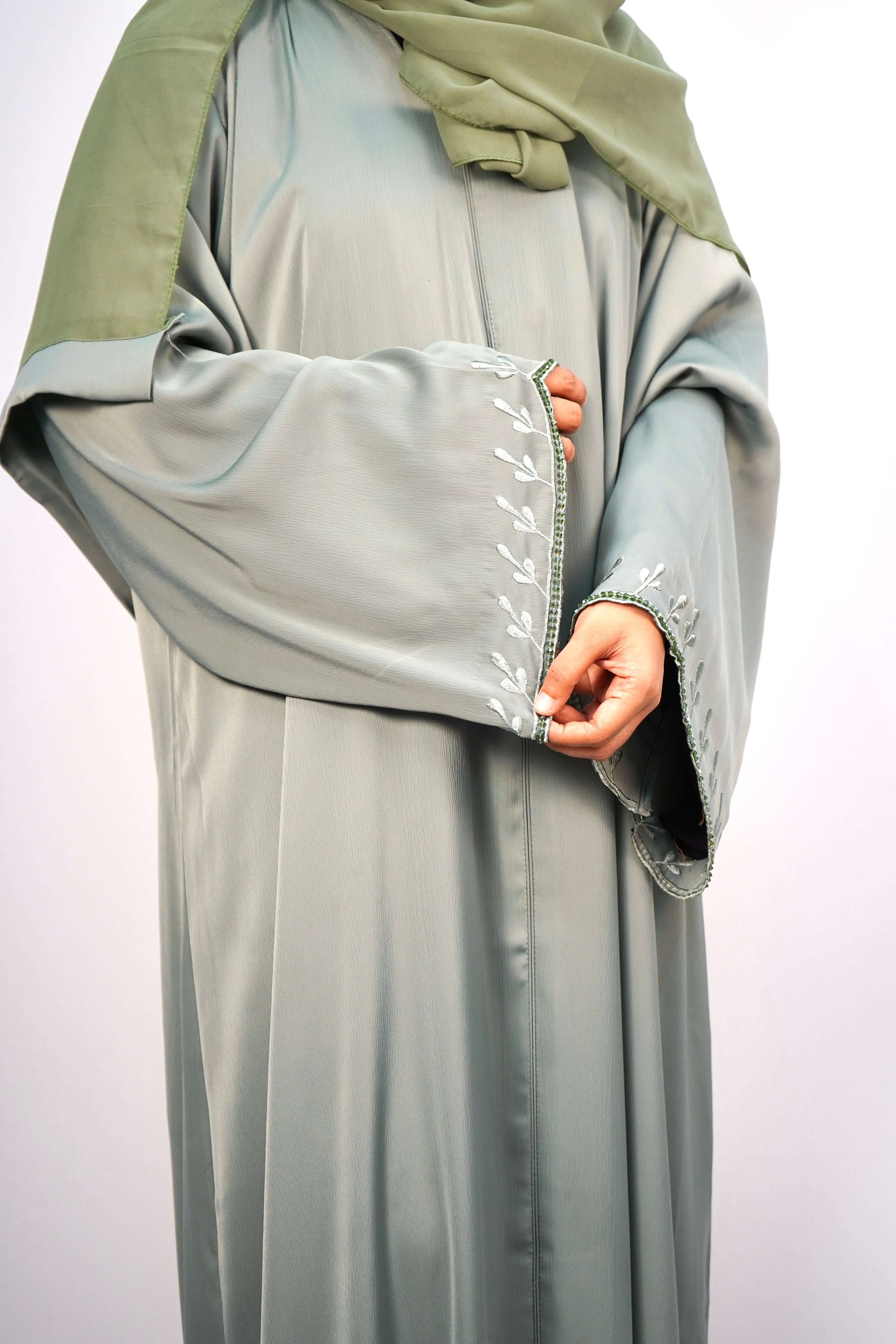 A close-up of the delicate, leaf-like embroidery and side slit on the hem of the green abaya.