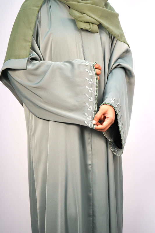 A close-up of the delicate, leaf-like embroidery and side slit on the hem of the green abaya.