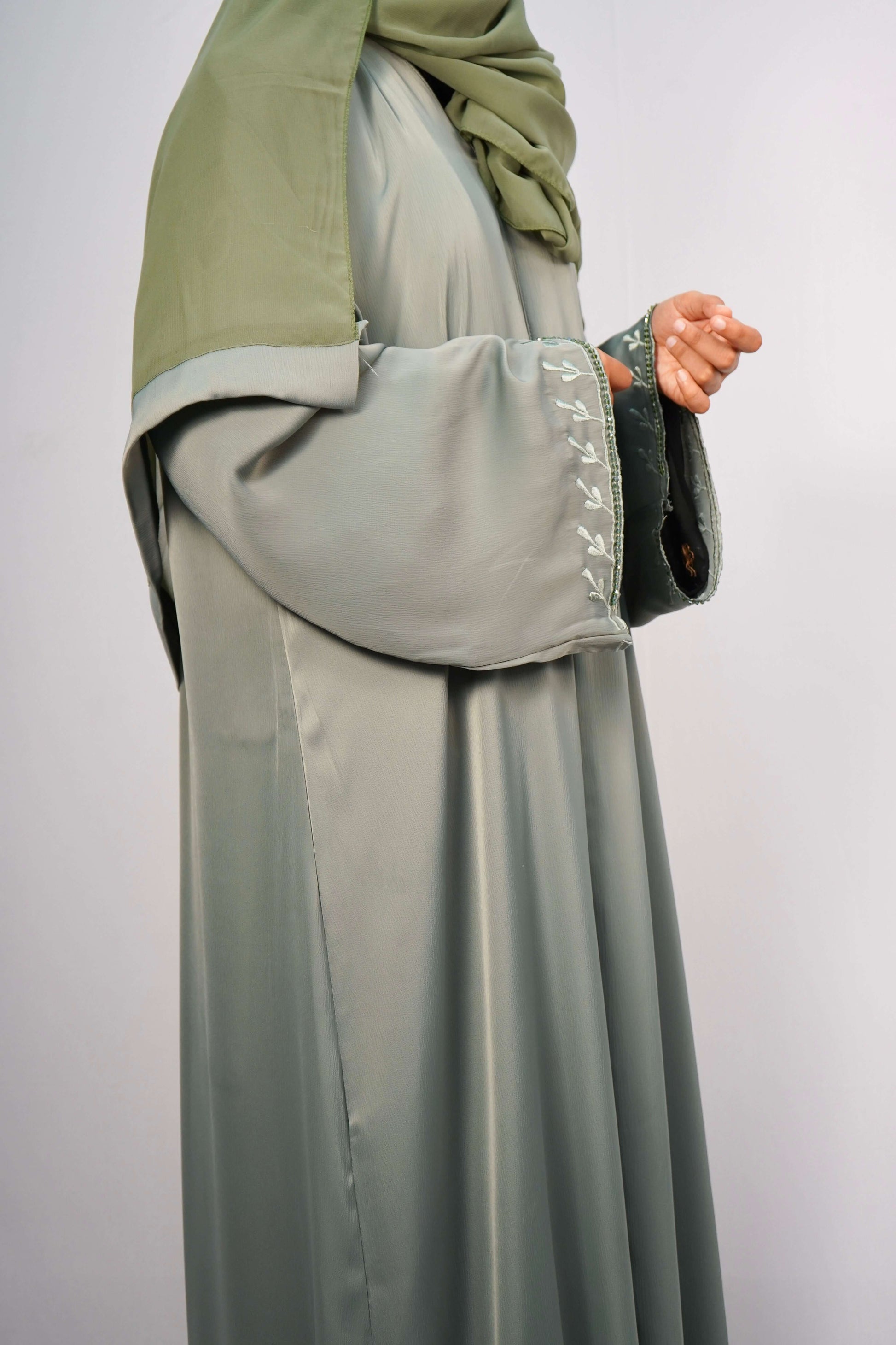 A side-on shot of the Tiktok Indonesian Abaya in sage green on a model, highlighting the elegant drape of the fabric and the detailed leaf-like embroidery on the sleeve.