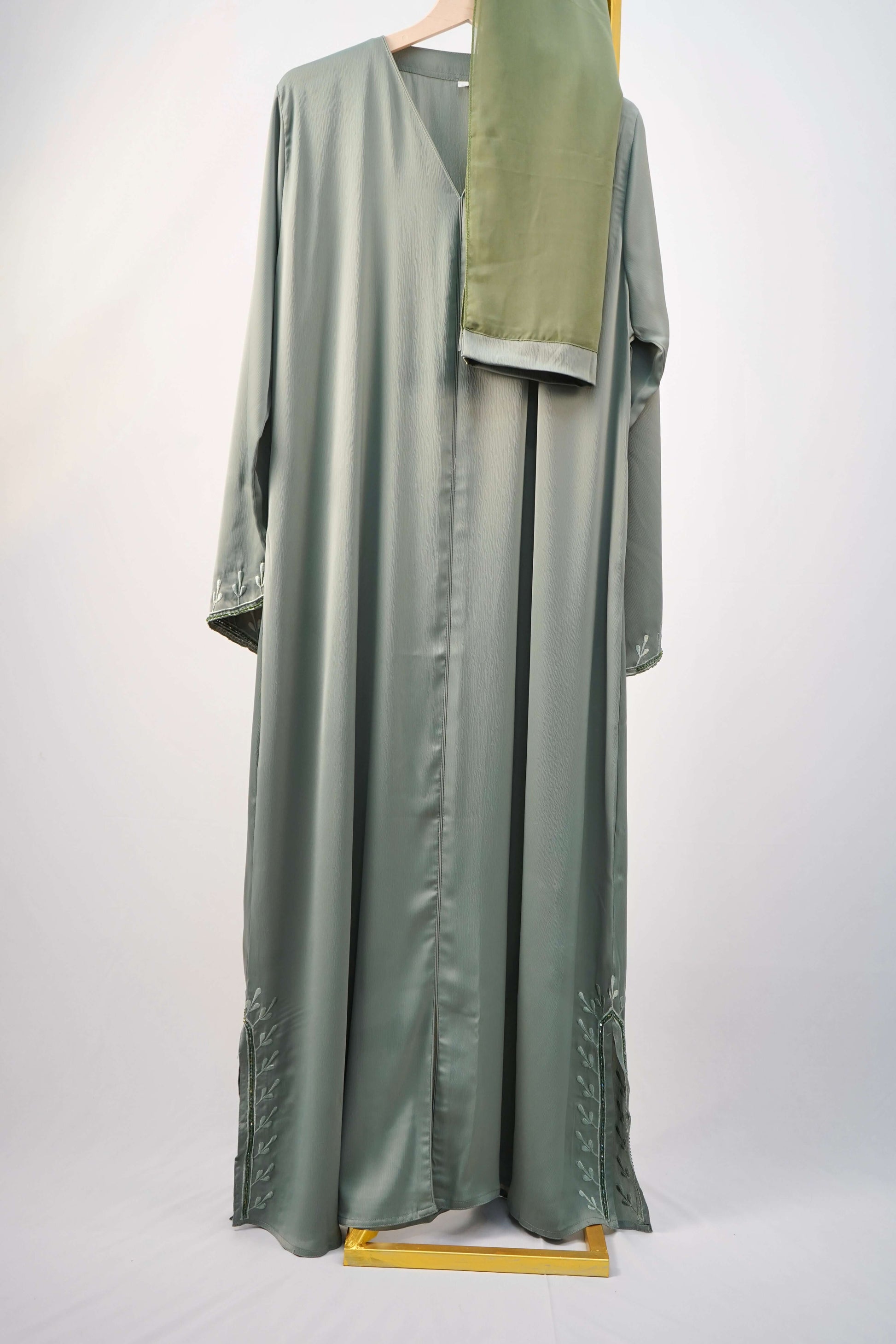 A full shot of the Tiktok Indonesian Abaya in sage green, hanging with its matching scarf.