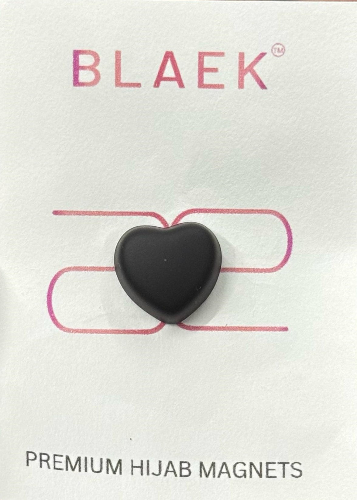 Black heart-shaped hijab magnet on premium packaging, placed on a neutral fabric.