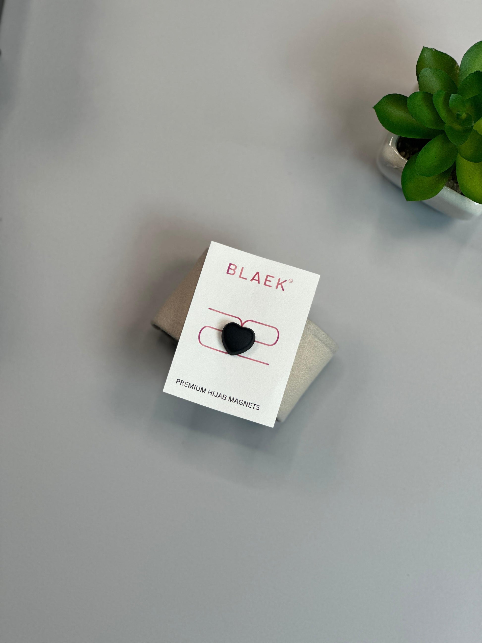 Premium heart-shaped hijab magnet in black, elegantly packaged and set against a modern backdrop.