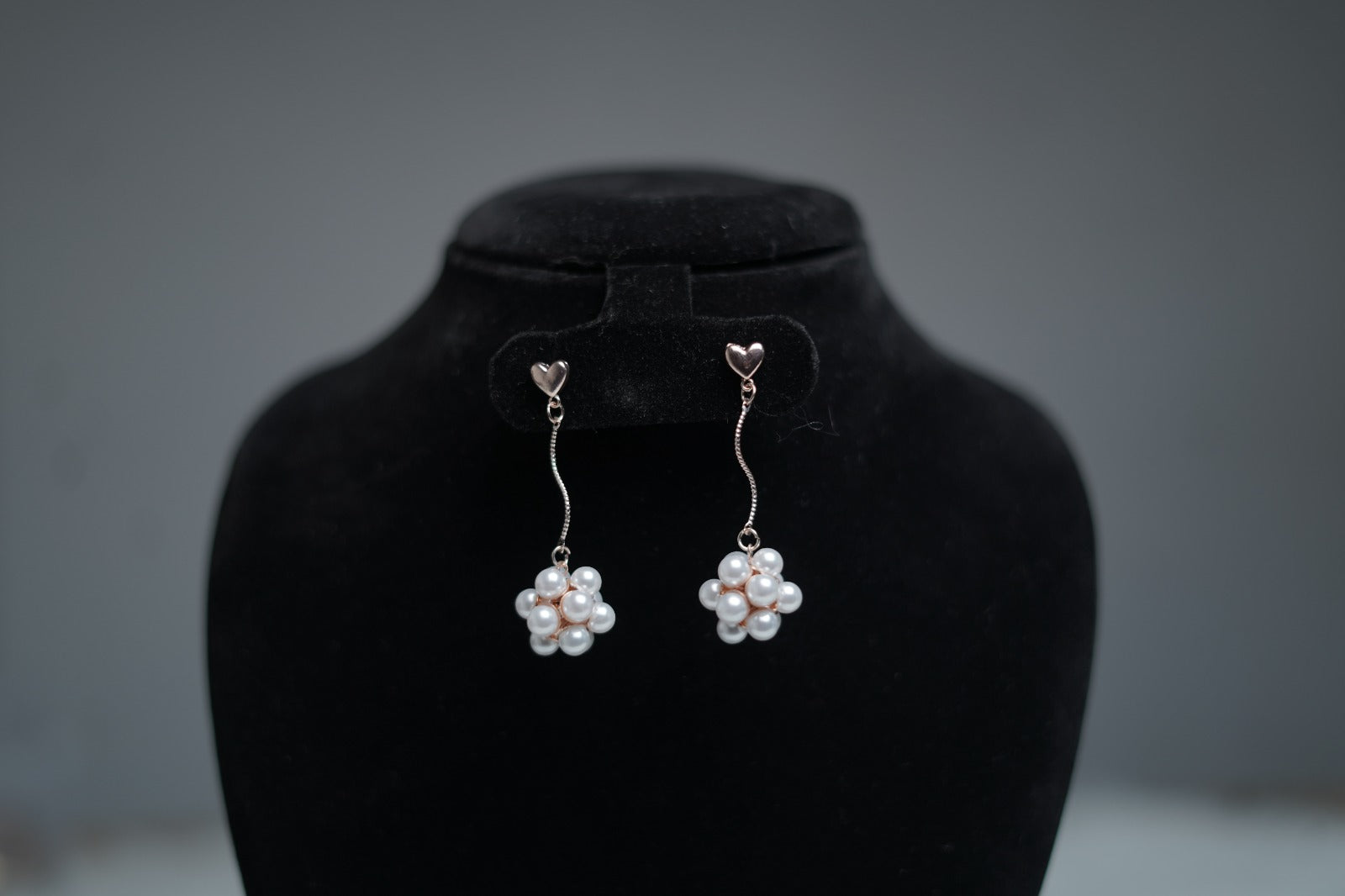 Heartlet pearl drop earrings with floral pearl cluster and rose gold heart studs on a black display.
