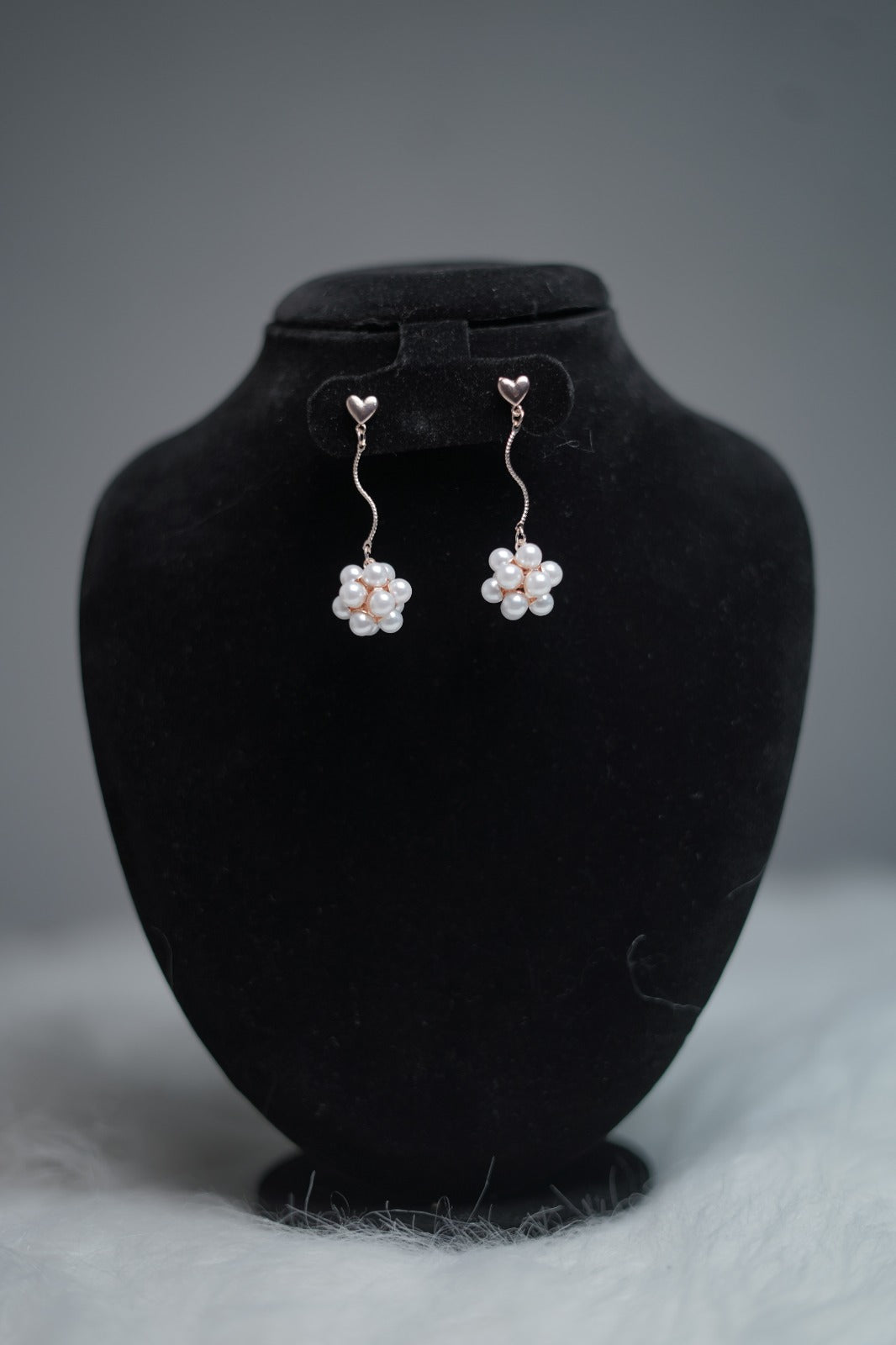 Dangling pearl earrings with mini heart studs and twisted drop design, displayed professionally.